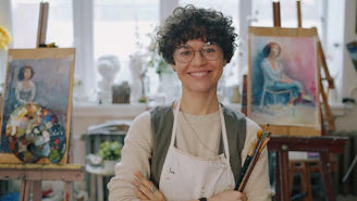 A woman with curly hair and glasses wearing an apron in an art studio