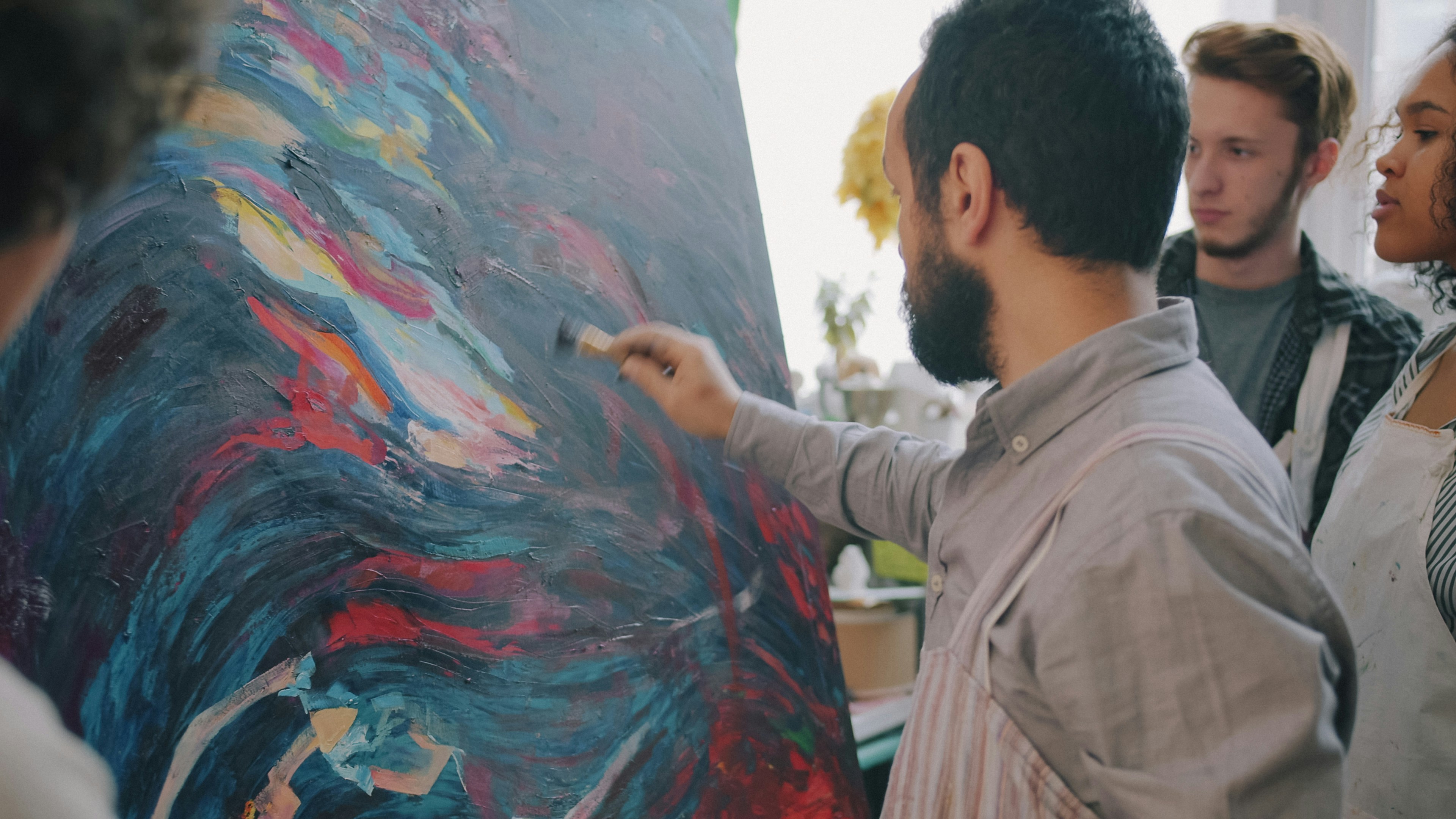 A man painting on a large canvas with two students watching in a studio