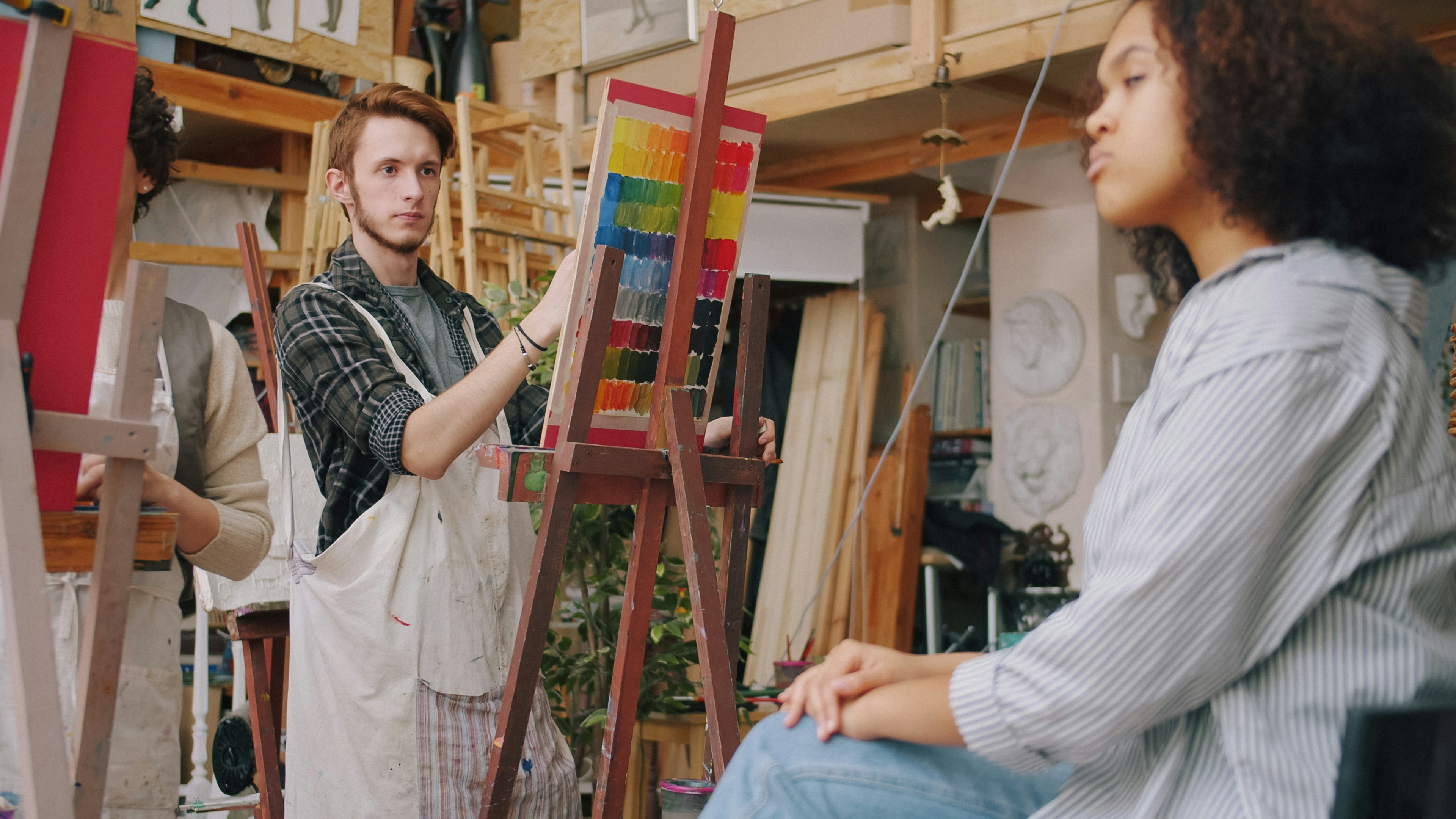 A man in an apron painting on a canvas in an art studio