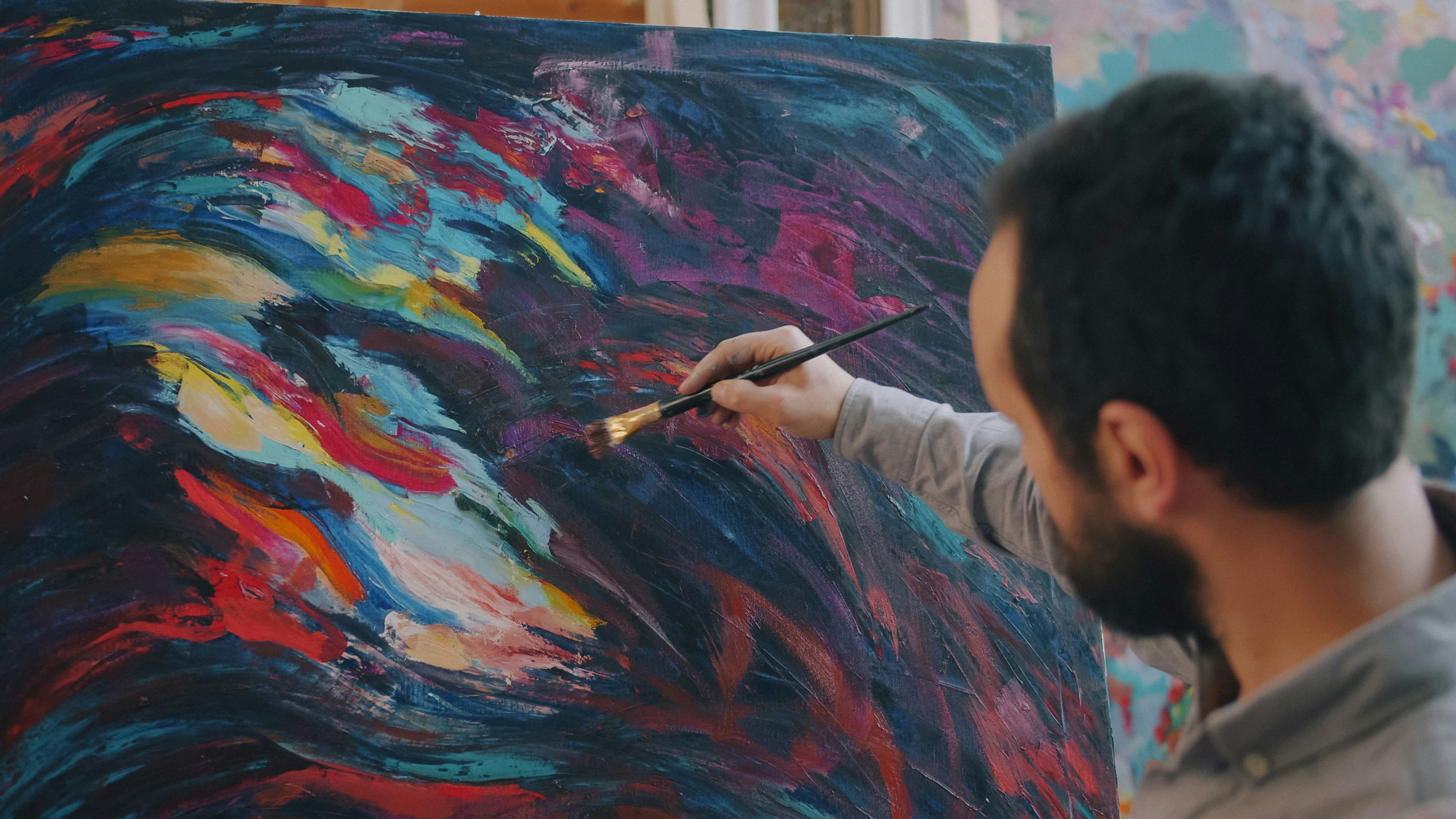 A person painting with a brush on a canvas with colorful abstract strokes