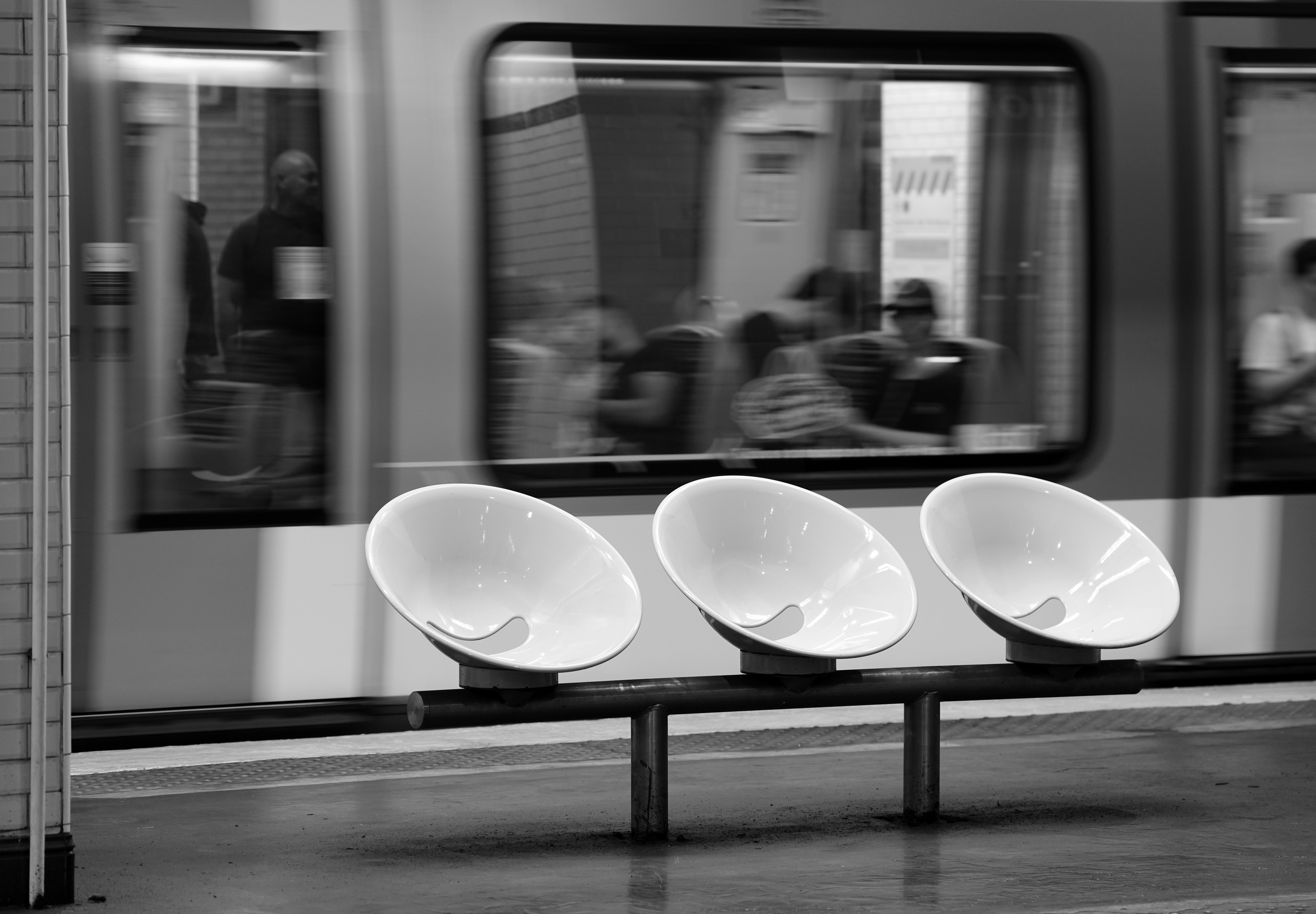 Three white bowl-shaped chairs on a platform with a blurred passing train