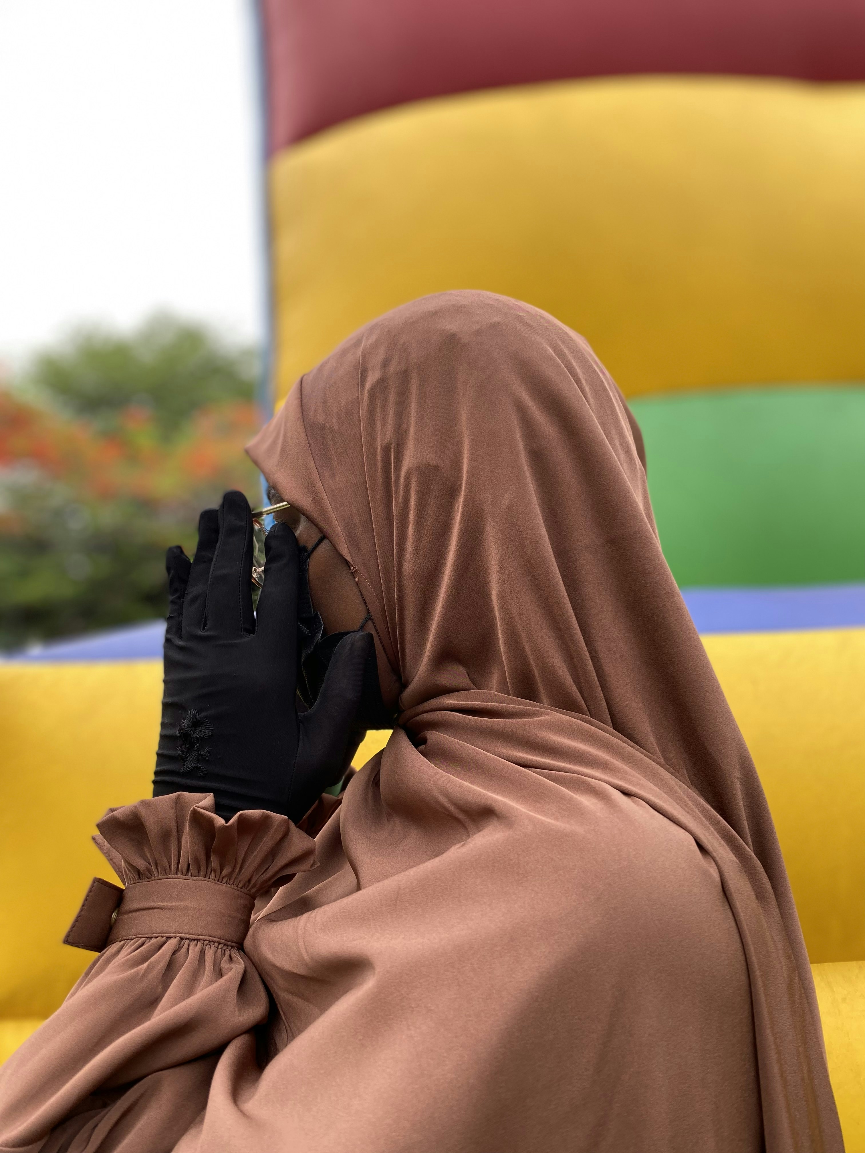 A person in a brown hijab and black gloves covering their face