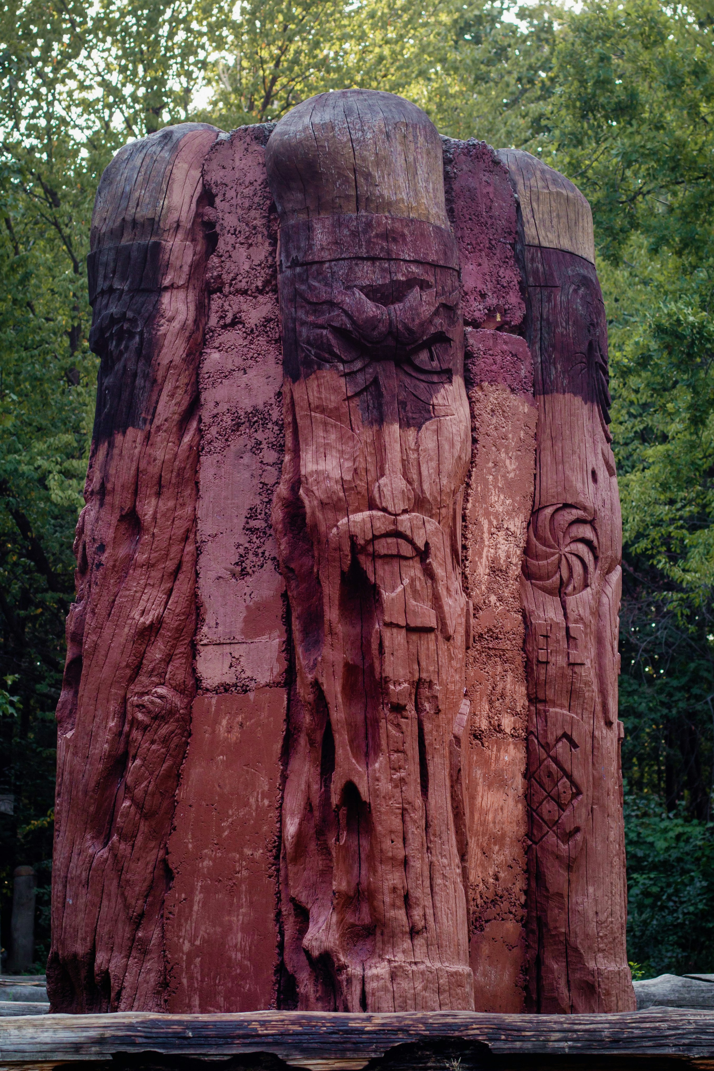A large wooden totem carved with a bearded face and symbols in a forest