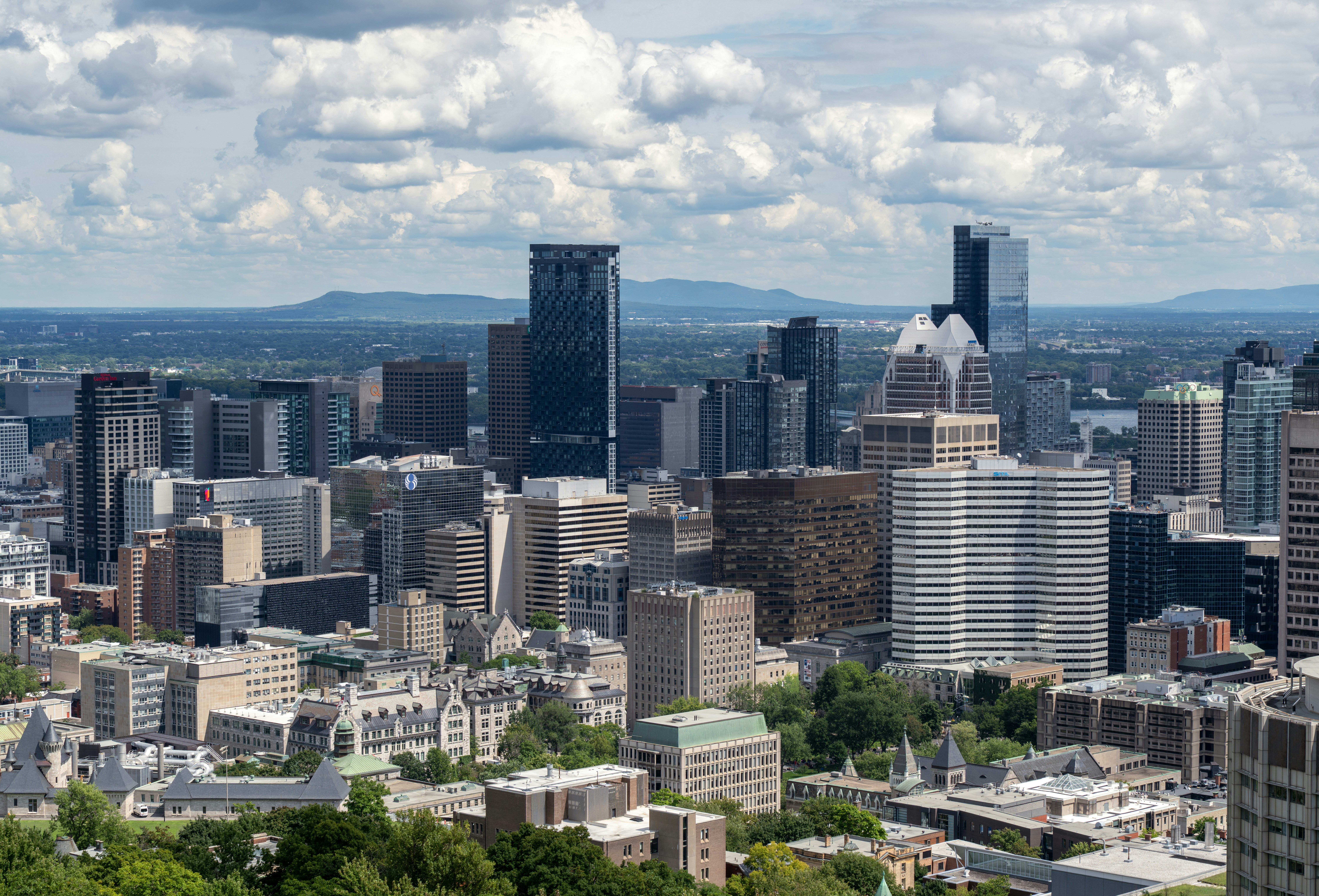 A dense city skyline with skyscrapers and distant mountains under a cloudy sky