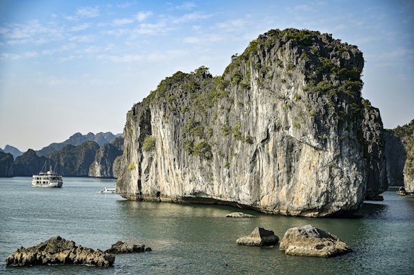 A cruise ship sailing past a large limestone karst in Ha Long Bay