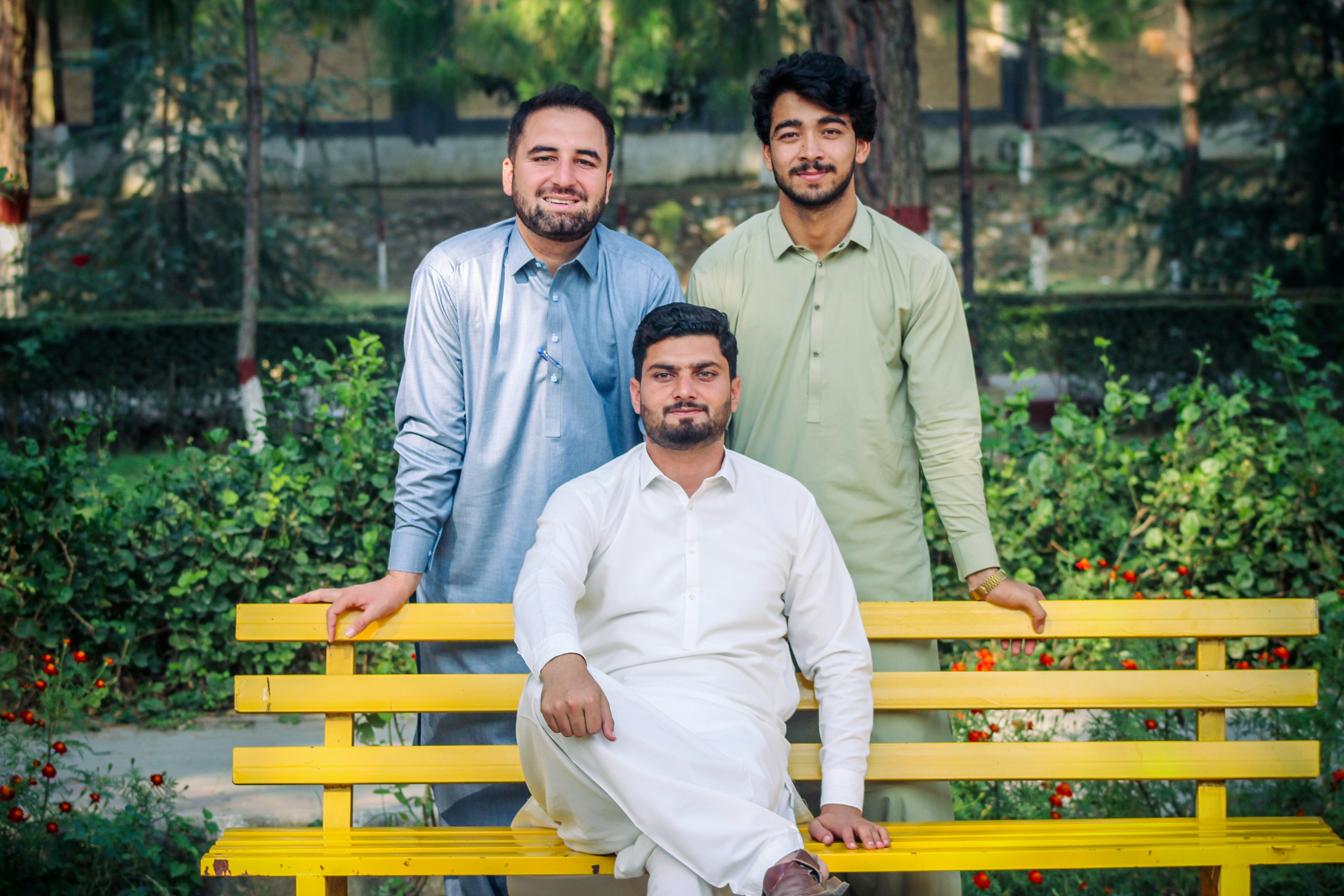 Three men in traditional shalwar kameez on a yellow bench in a park