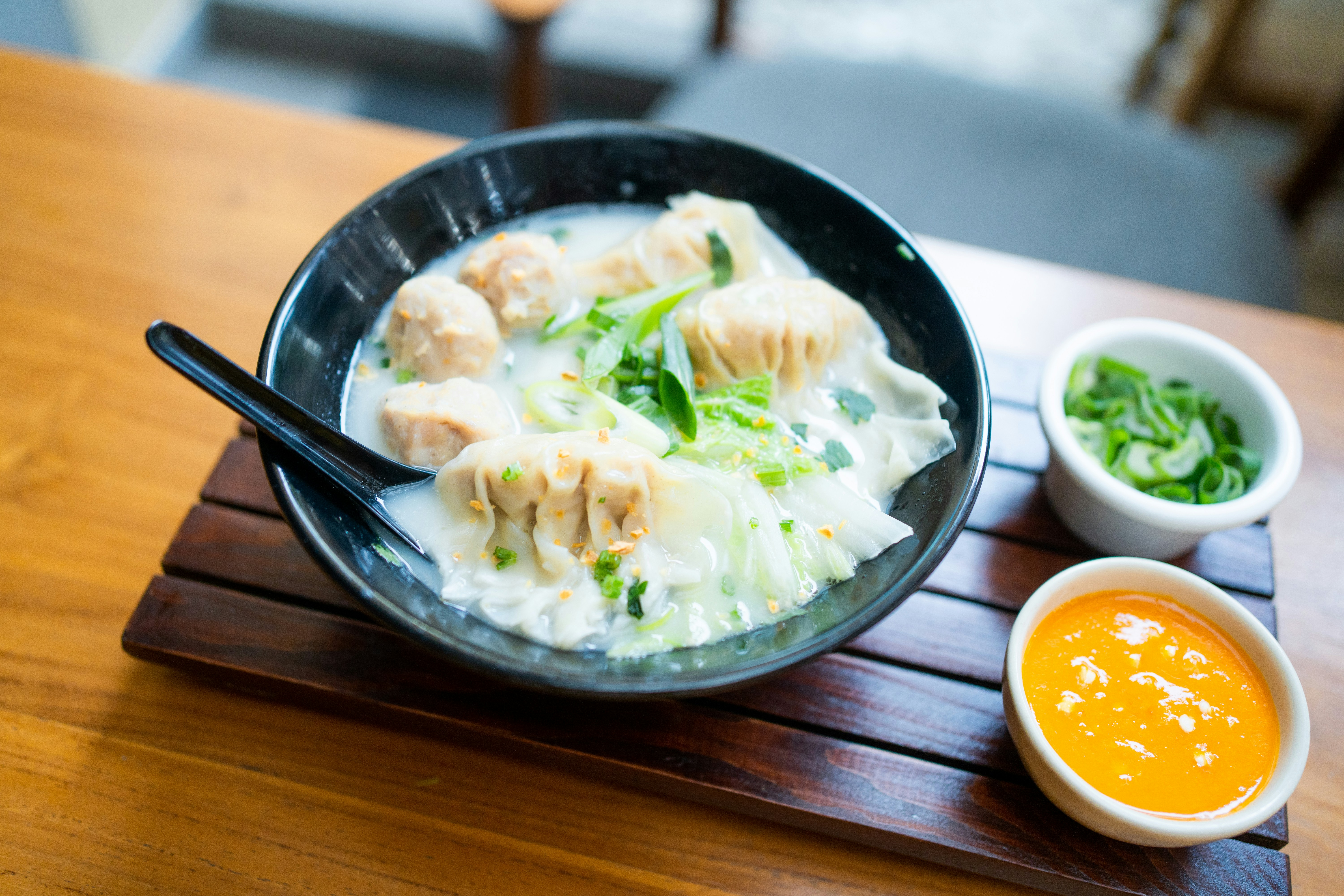 A bowl of wonton soup with meatballs and greens on a wooden tray