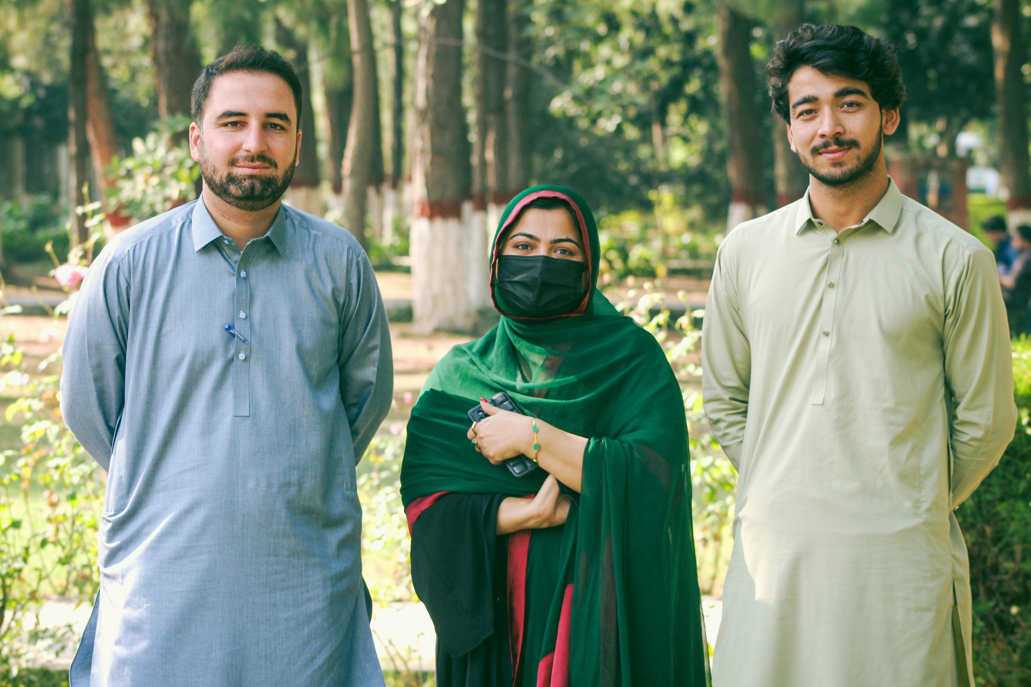 Two men and a woman in a headscarf and mask standing in a park