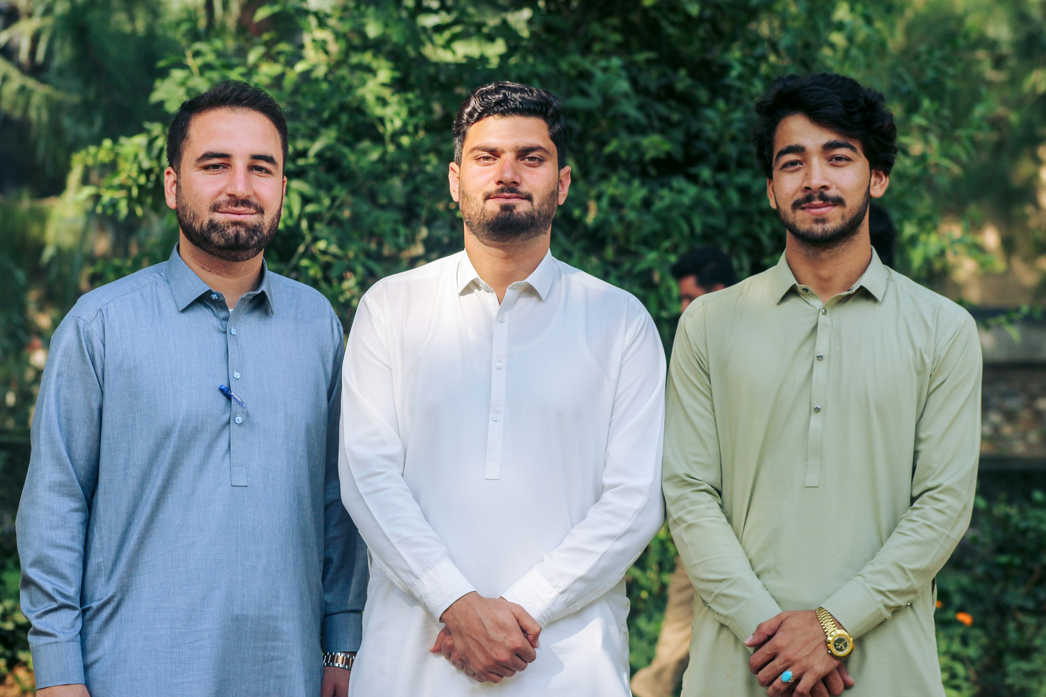 Three men in traditional shalwar kameez standing together in a garden