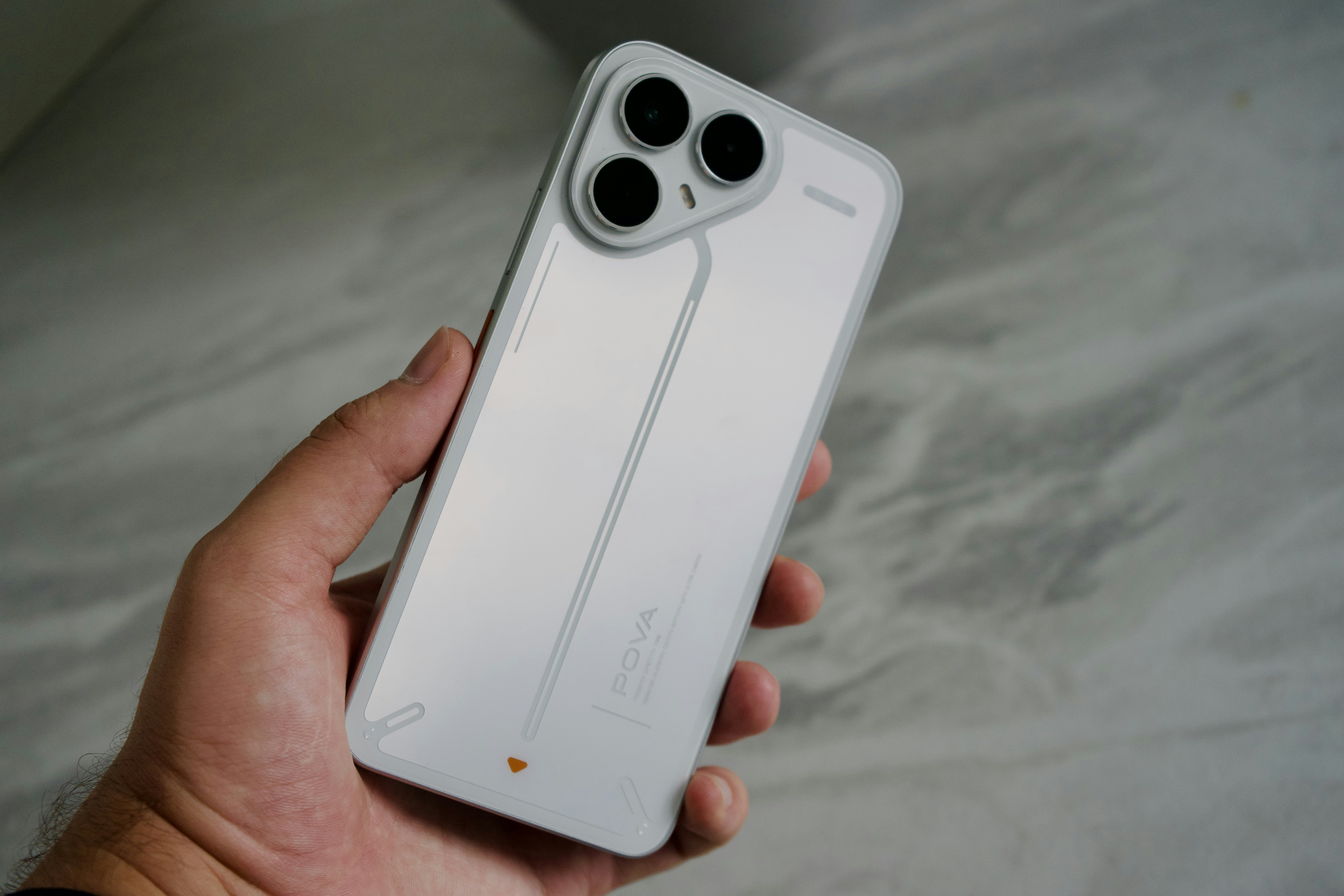 A hand holding a white smartphone with three camera lenses on a grey surface