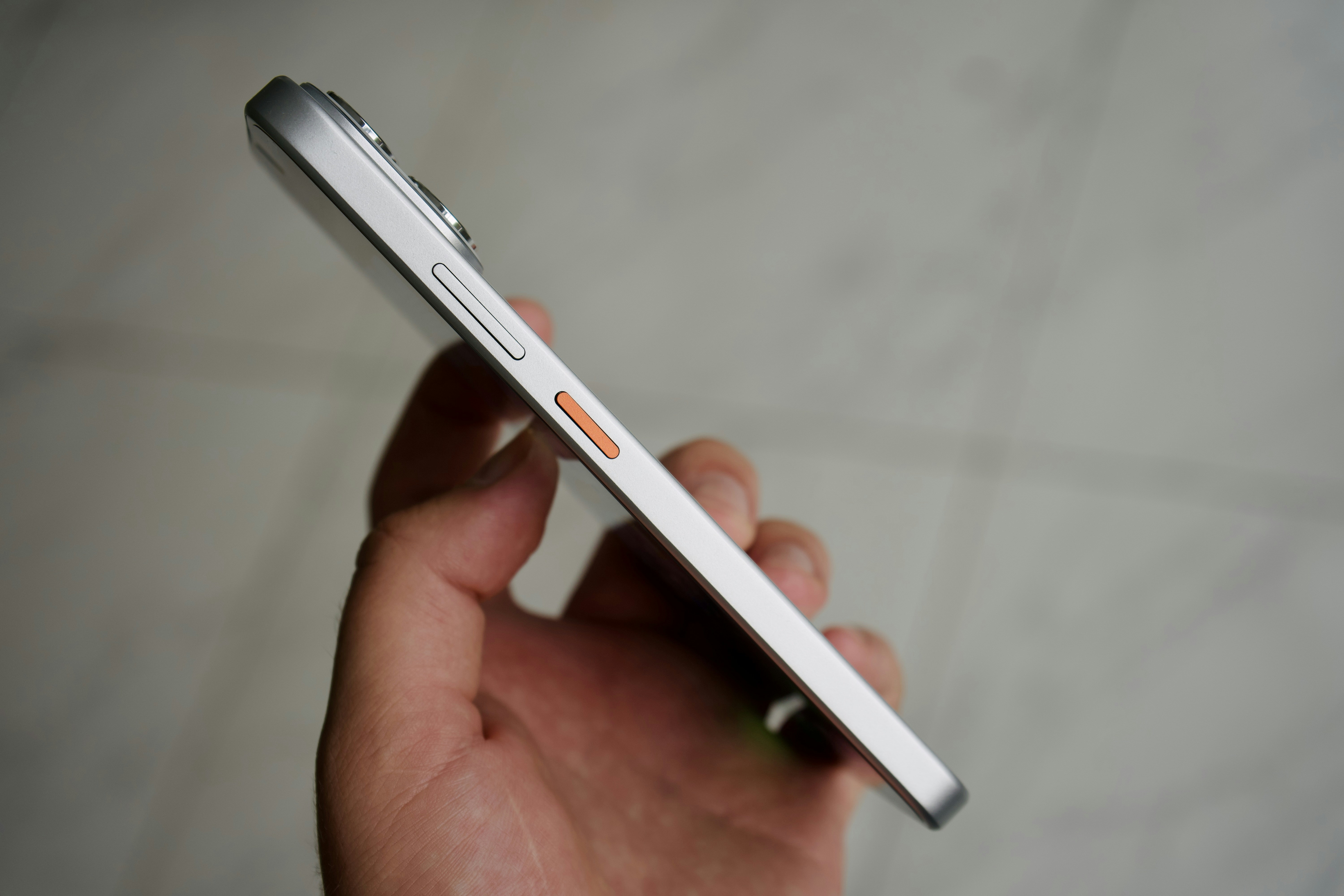 A hand holding a silver smartphone with a prominent orange power button
