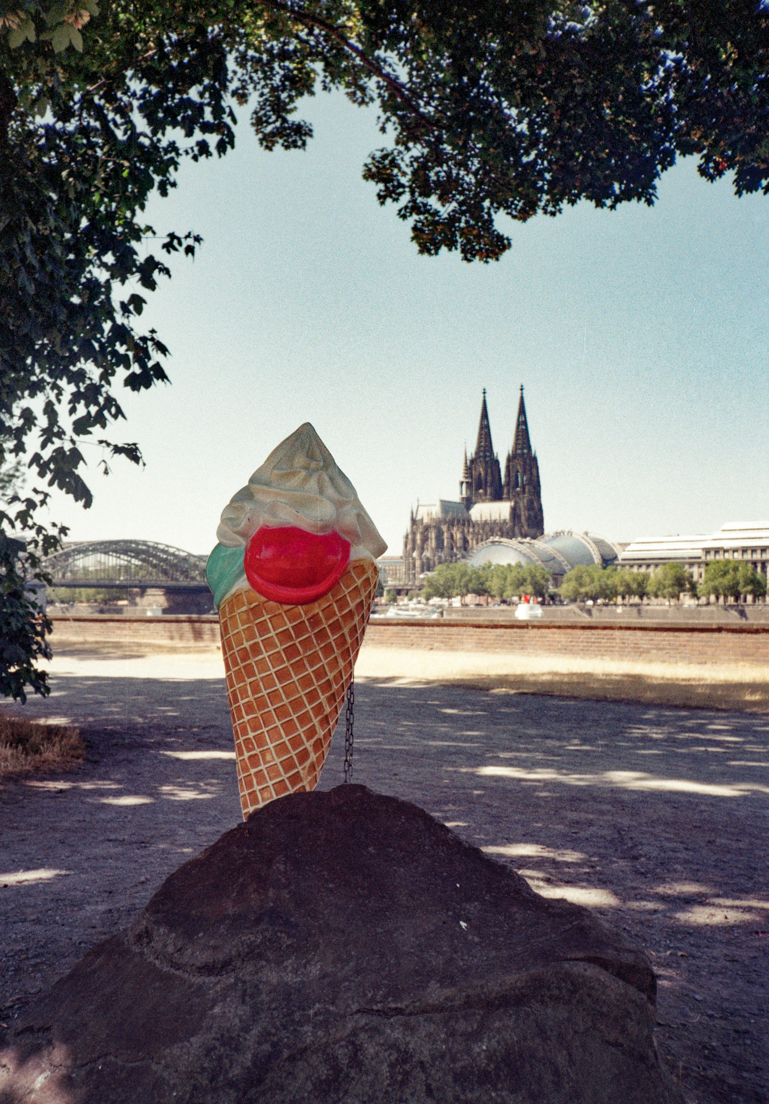 A large ice cream cone sculpture on a rock with Cologne Cathedral in the background