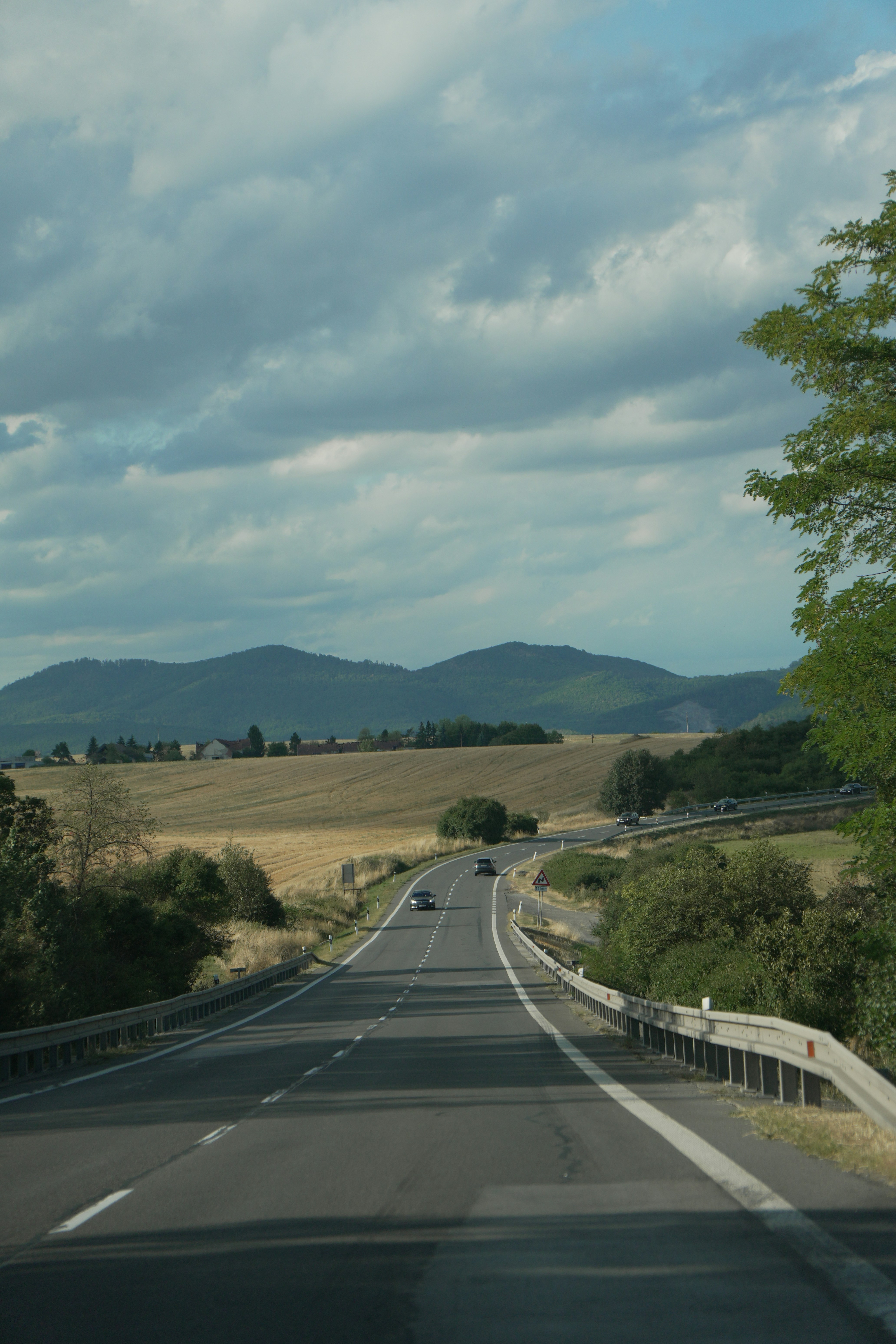A winding road through a rural landscape with rolling hills under a cloudy sky