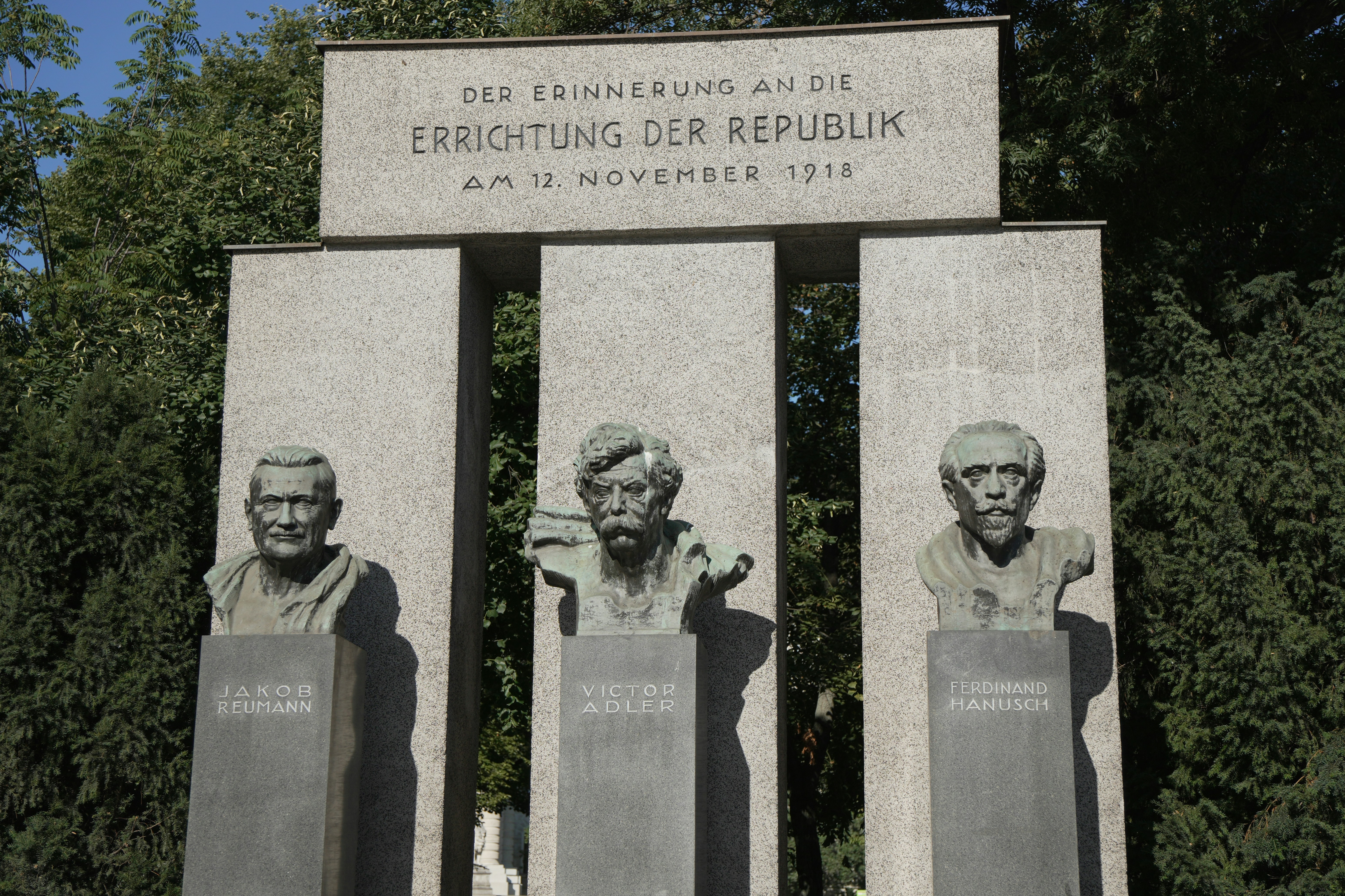 Three bronze busts on stone pedestals before a monument in Vienna, Austria