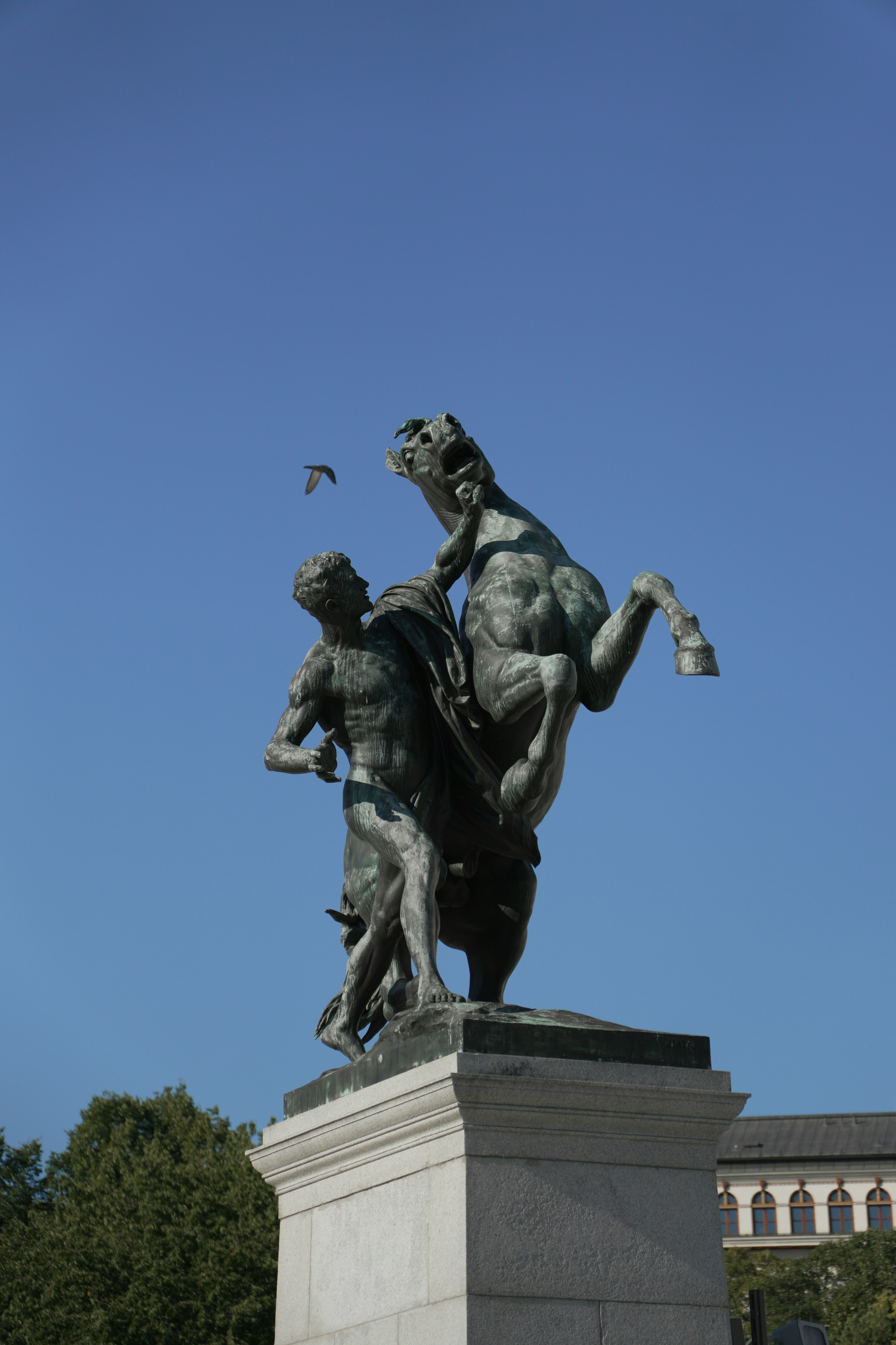 A bronze statue of a man restraining a rearing horse against a blue sky