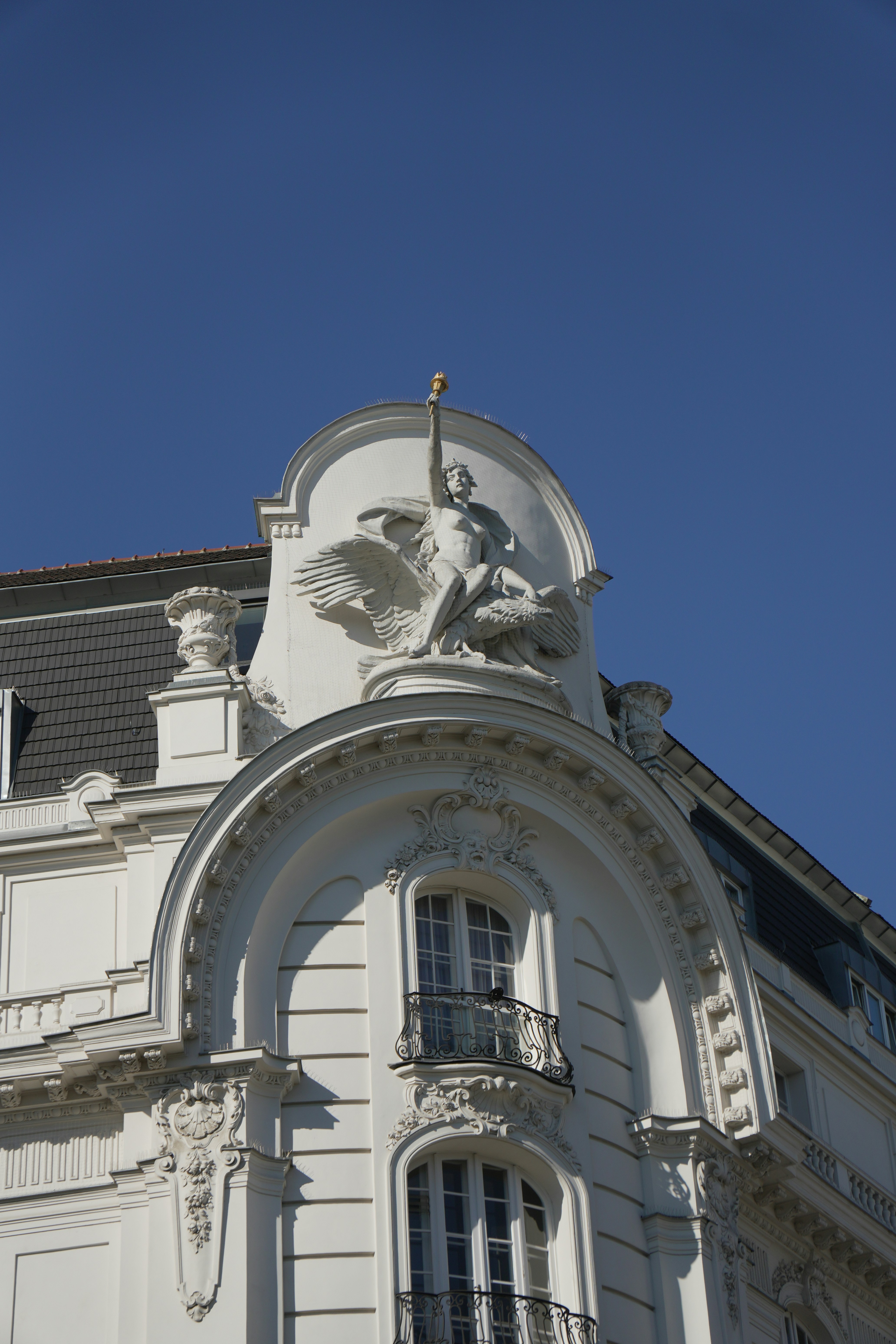 A white stone sculpture of a winged figure holding a torch on a building