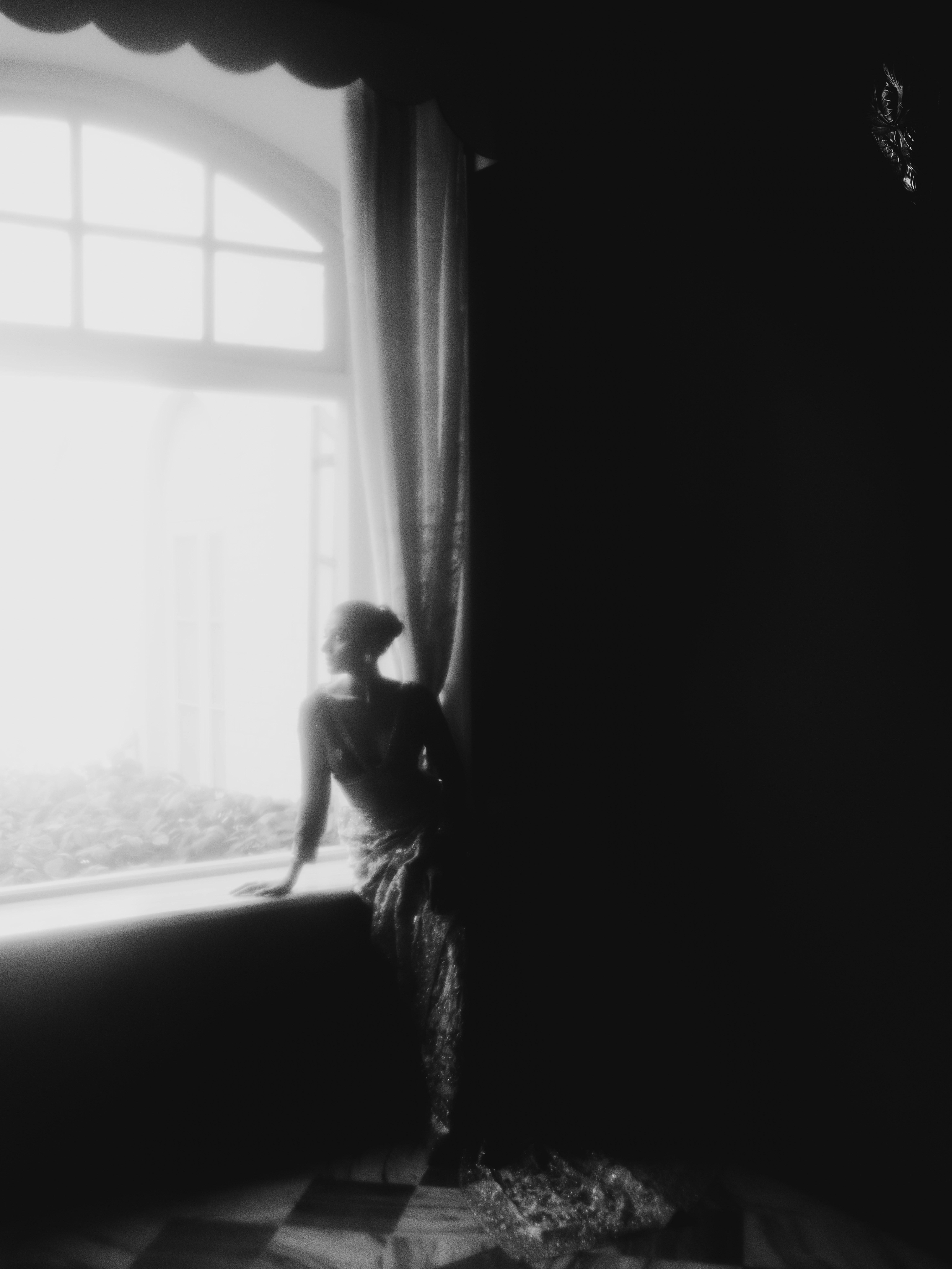 A person in a sari silhouetted against a bright window in a dark room
