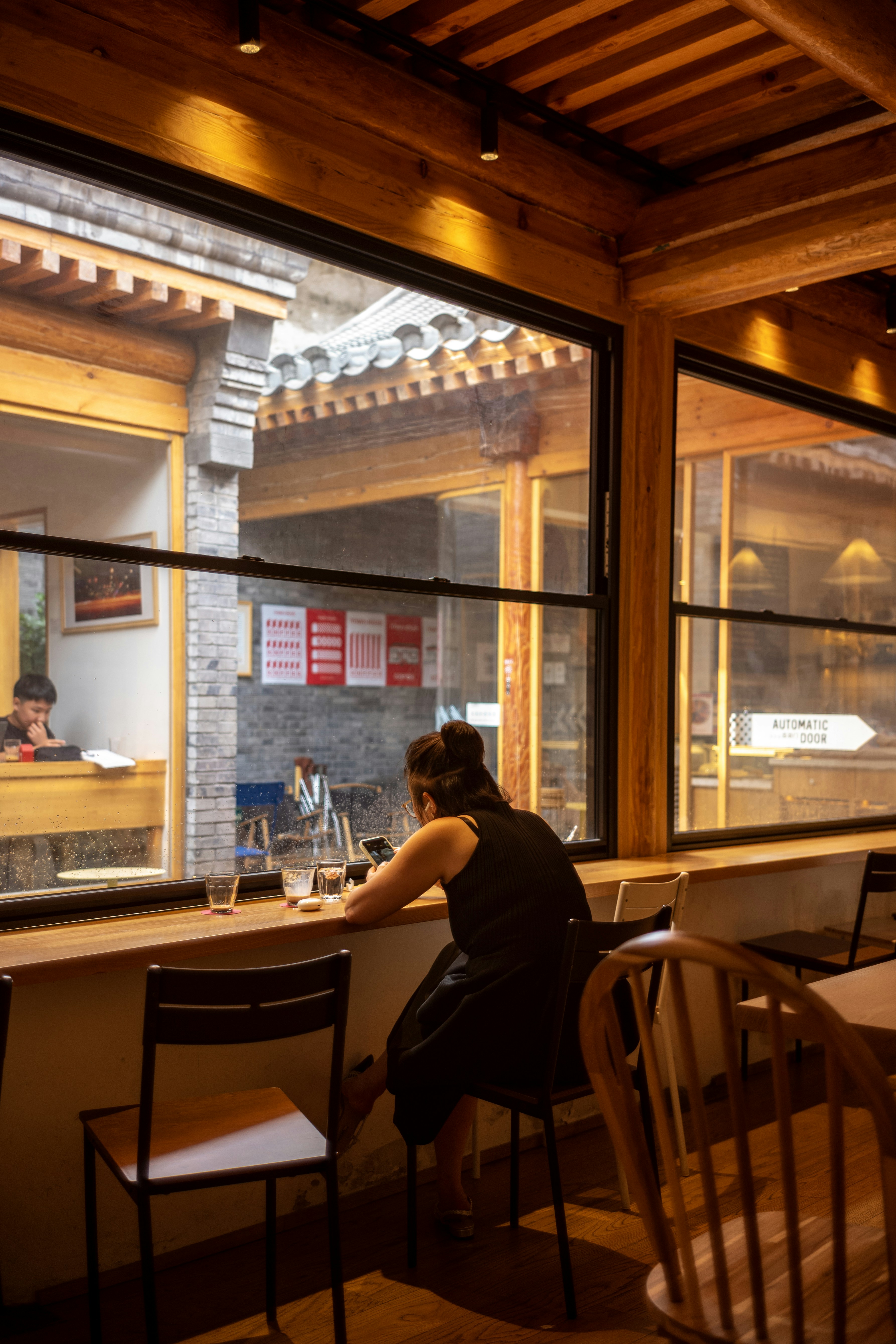 A woman in a black dress using a smartphone at a cafe window