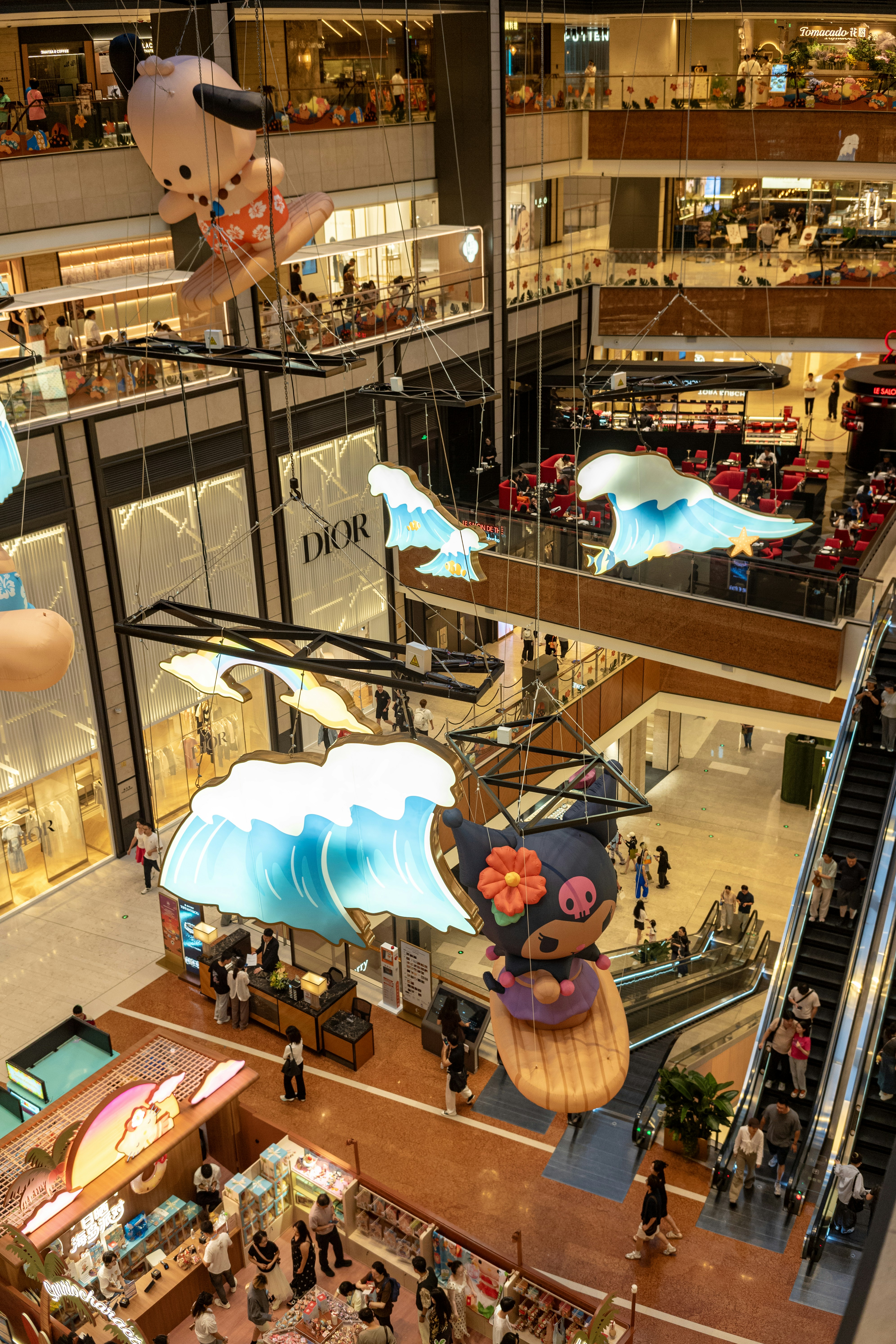 Inflatable cartoon characters on surfboards suspended in a multi-level shopping mall atrium