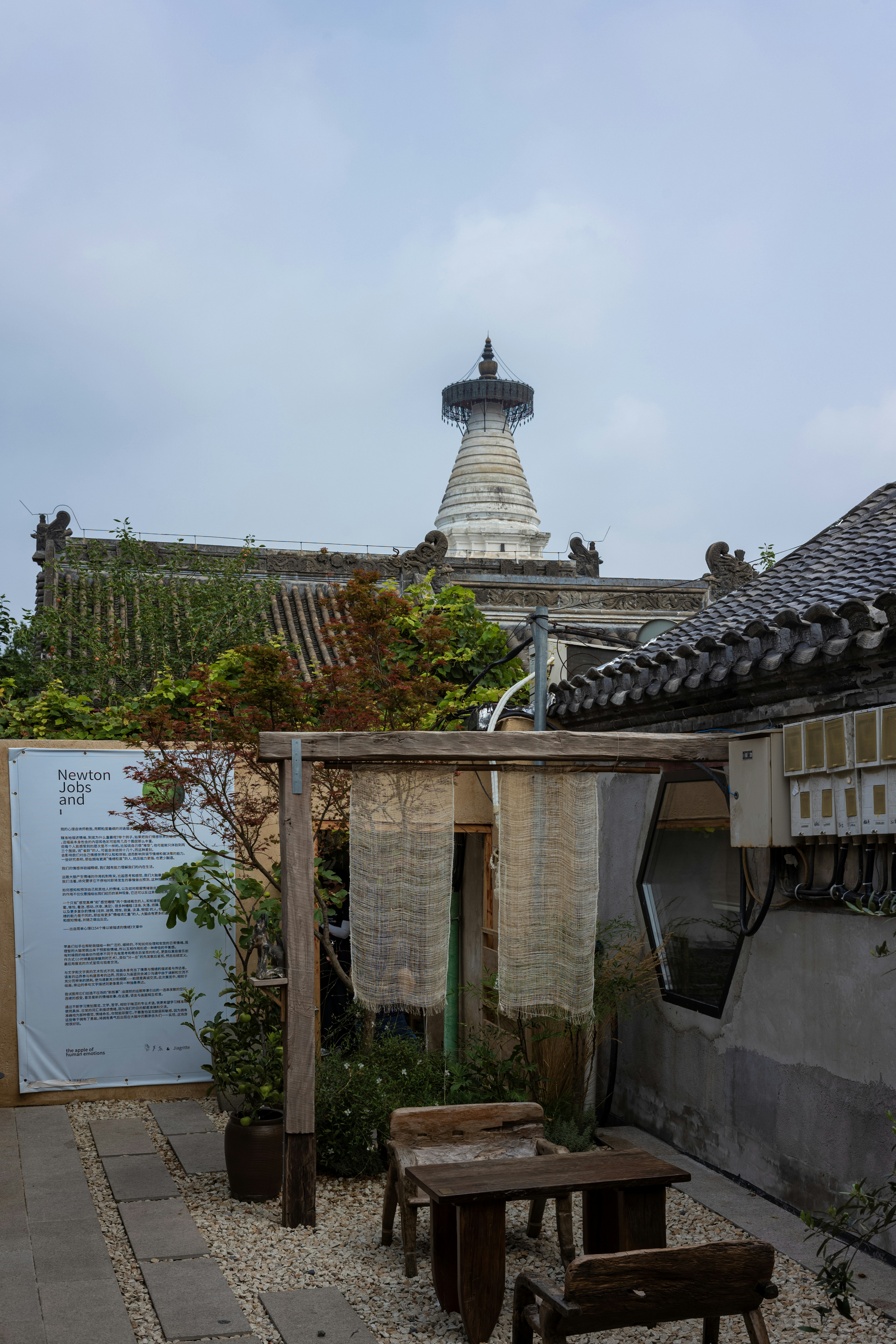 A white pagoda rising above traditional tiled roofs in a courtyard with wooden furniture