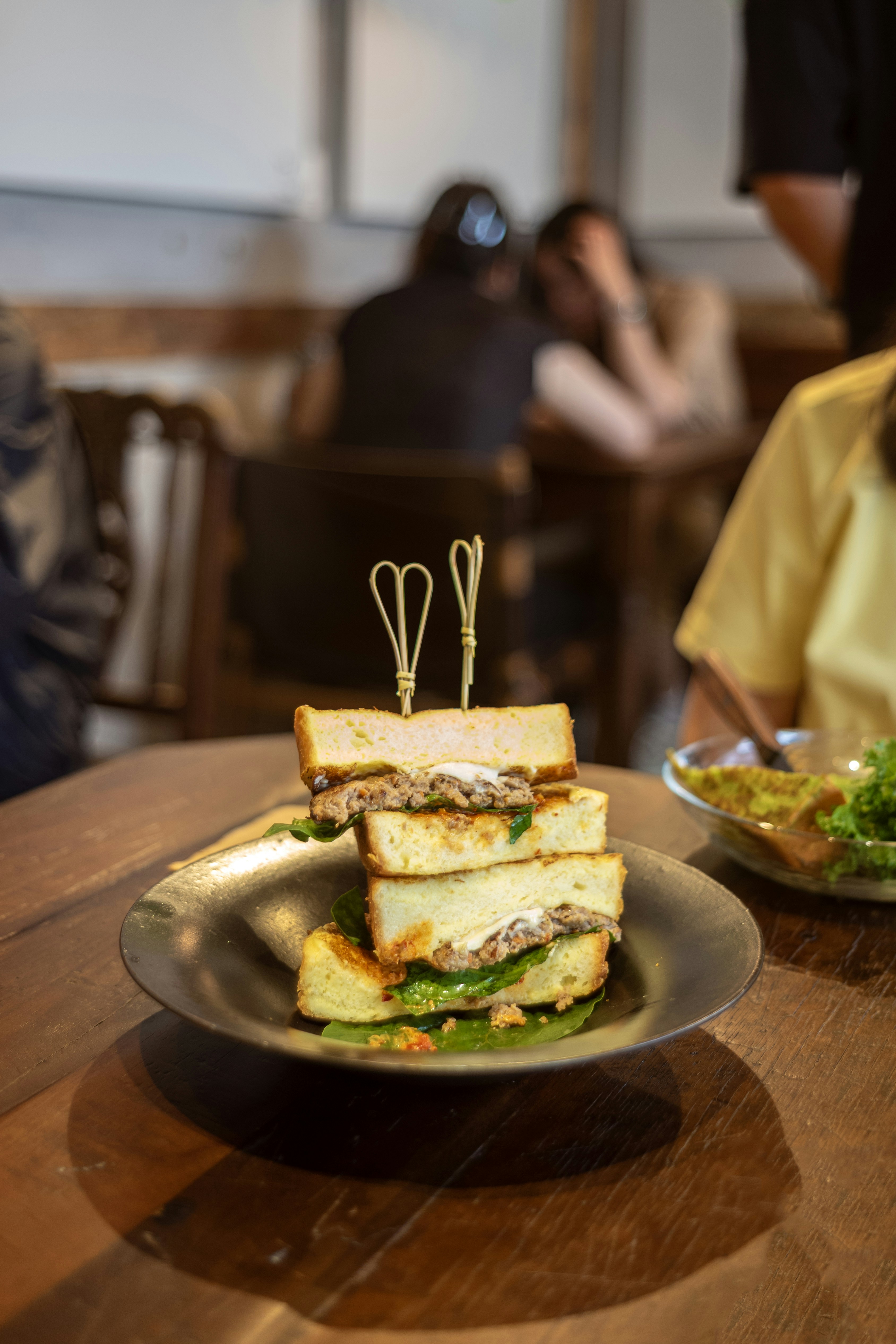 A stacked sandwich with meat and greens on a black plate in a restaurant