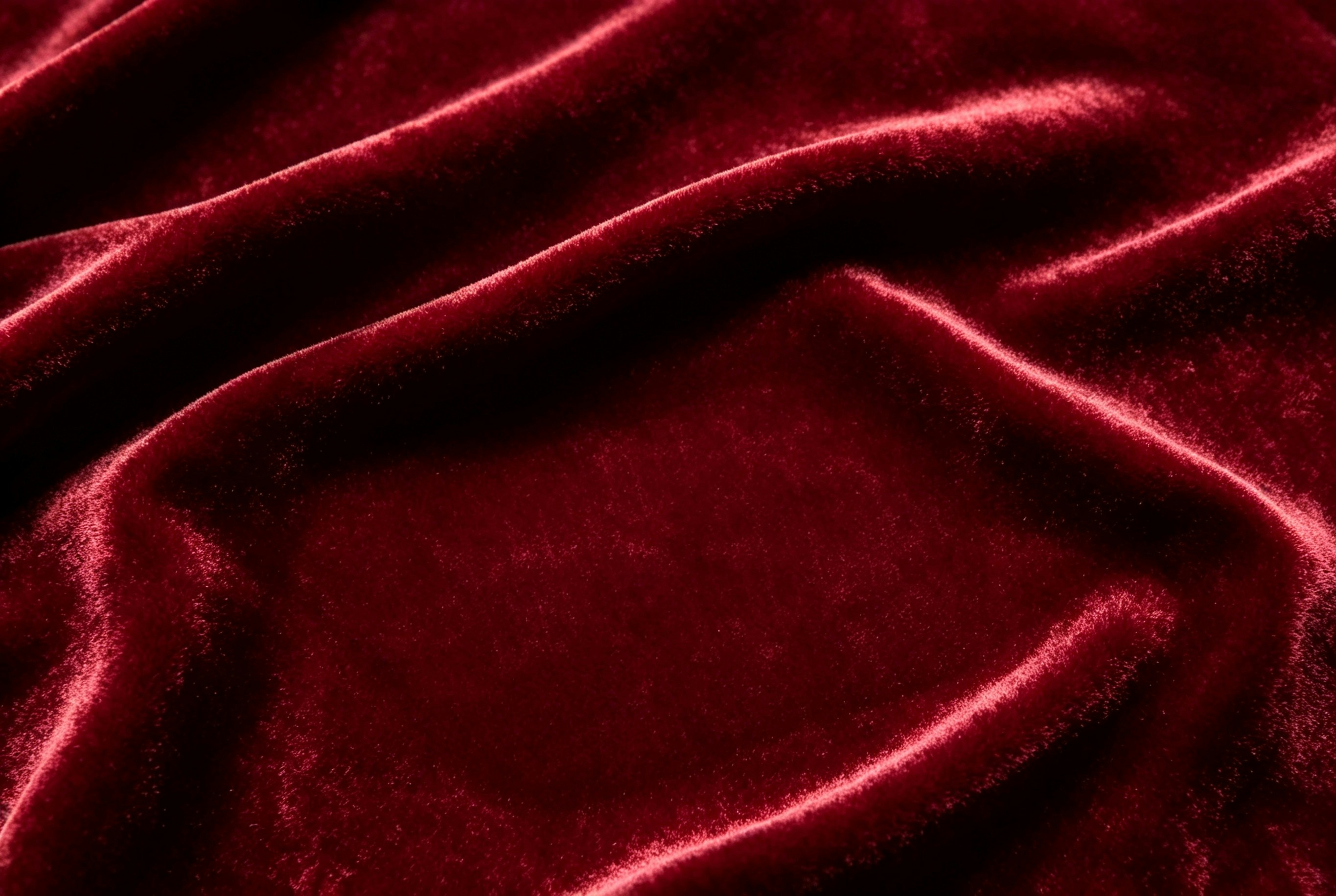 Deep red velvet fabric with soft folds and light reflecting on the surface