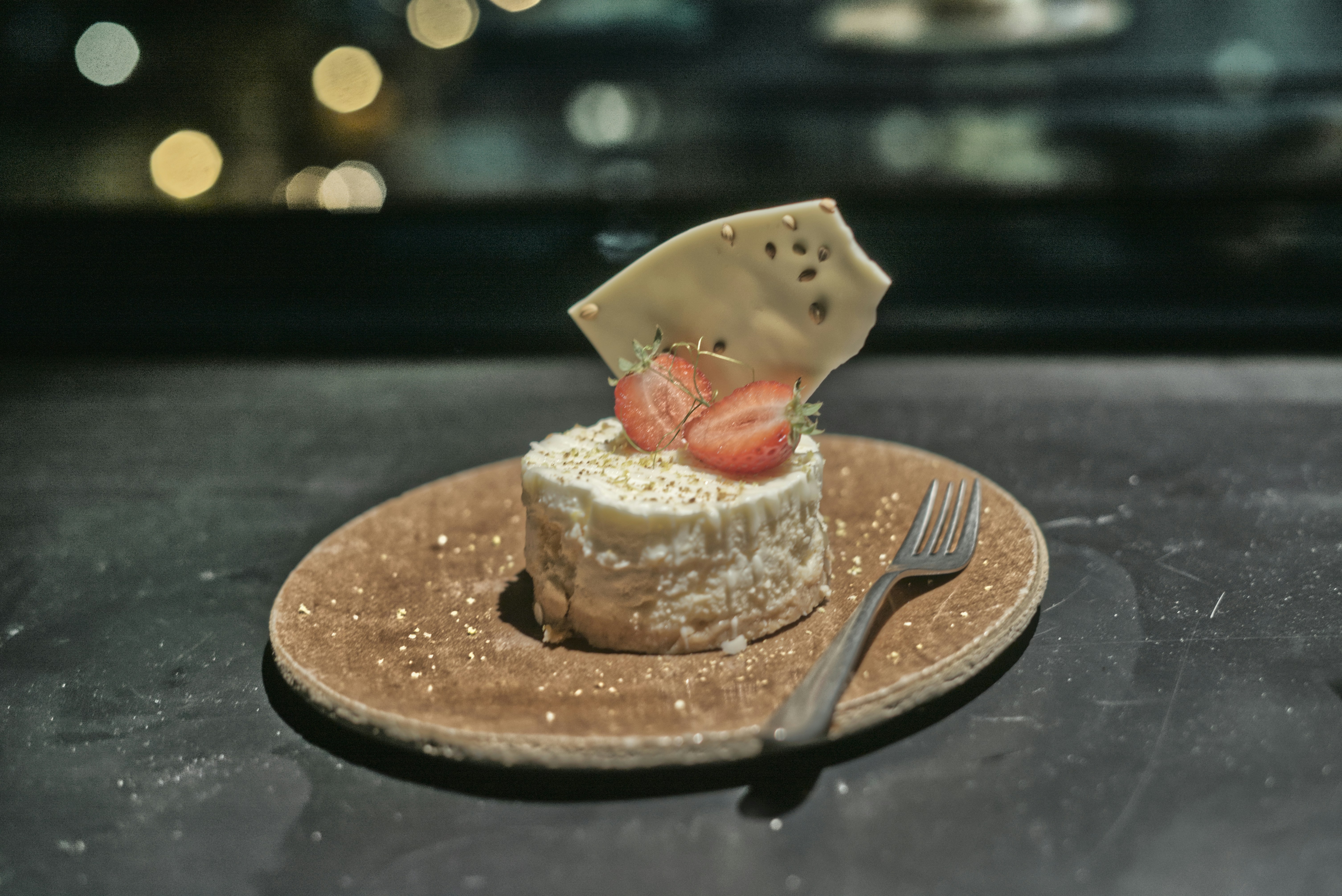 A small white dessert topped with strawberries and a chocolate shard on a plate