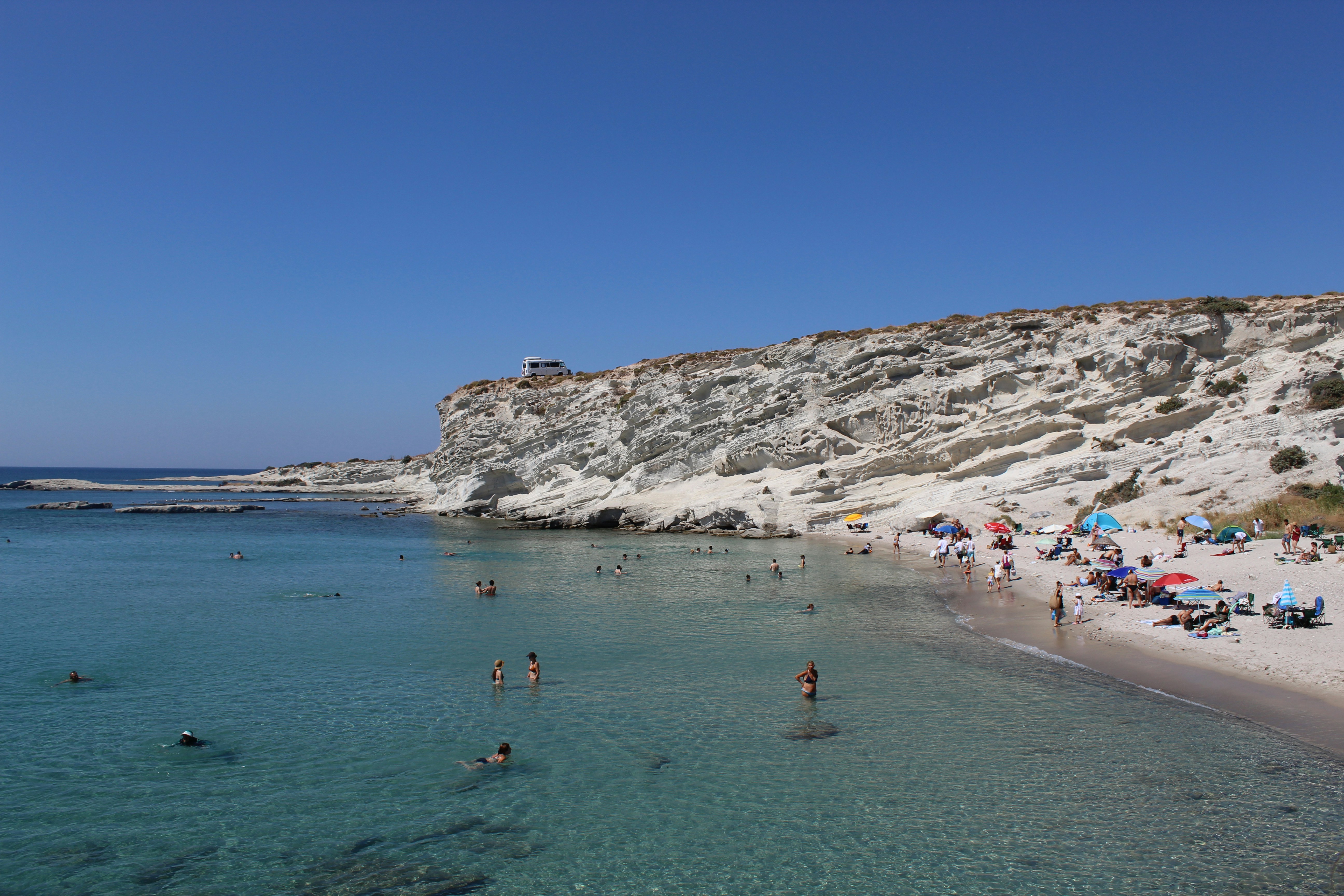 People swimming in clear turquoise water beside a white rocky cliff and beach