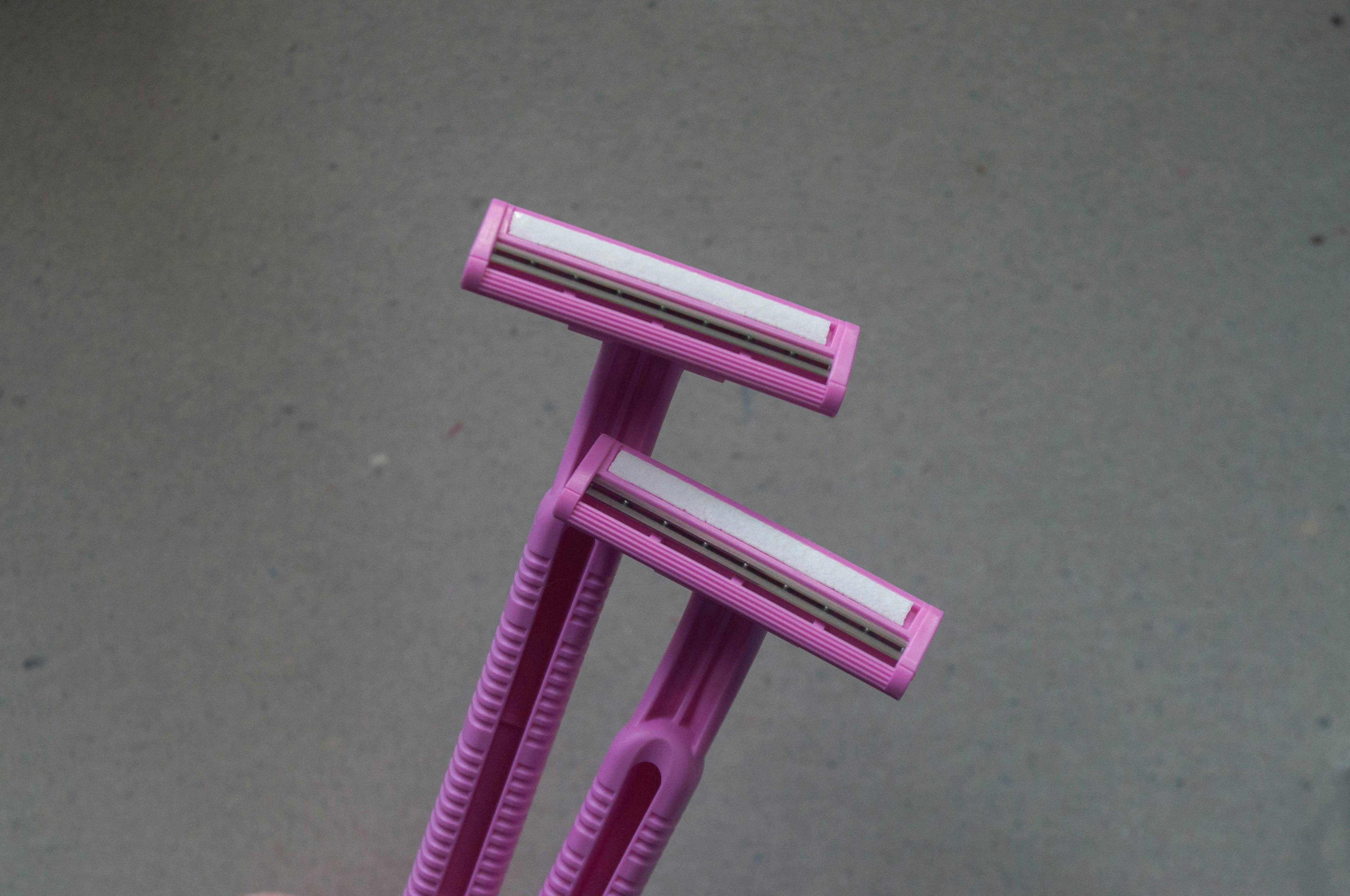 Two pink disposable razors held against a plain grey background