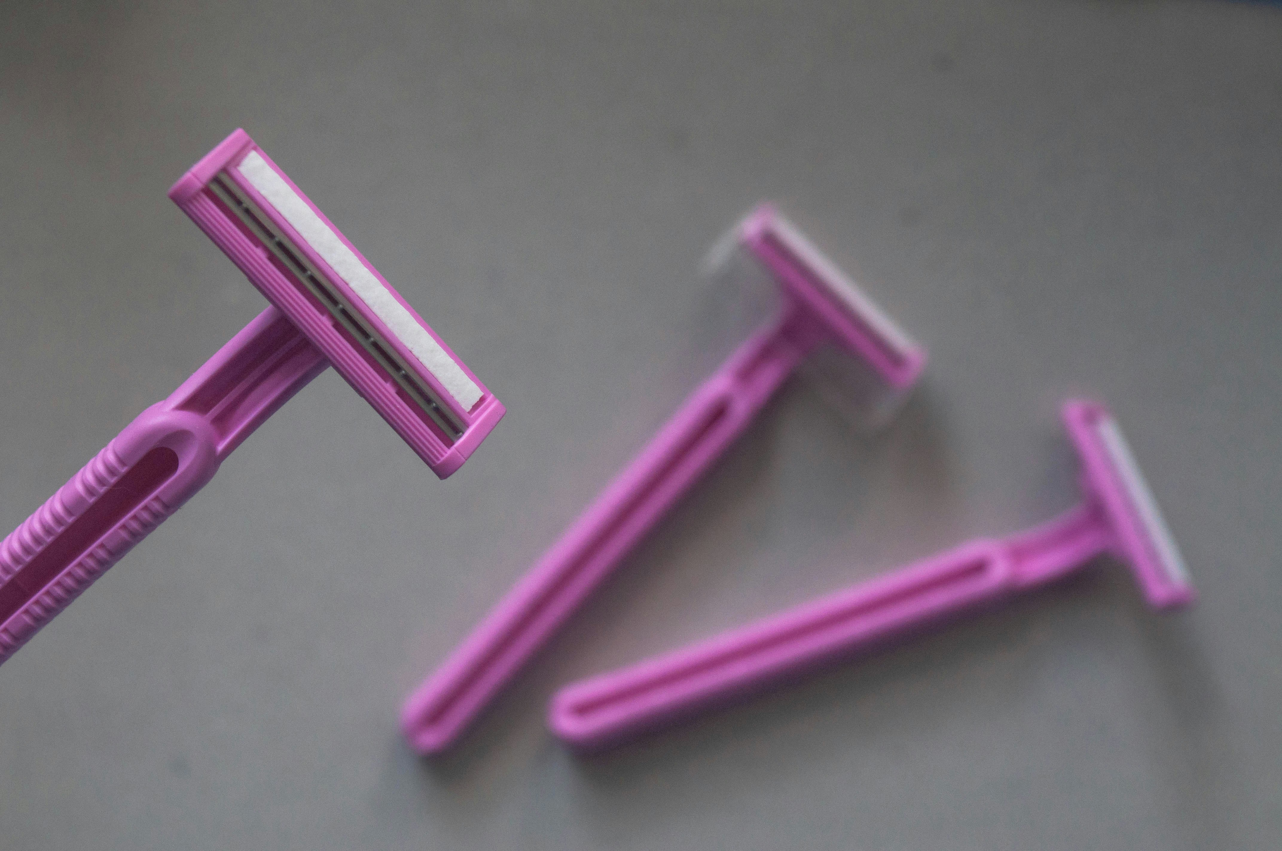Three pink disposable razors arranged on a plain grey surface
