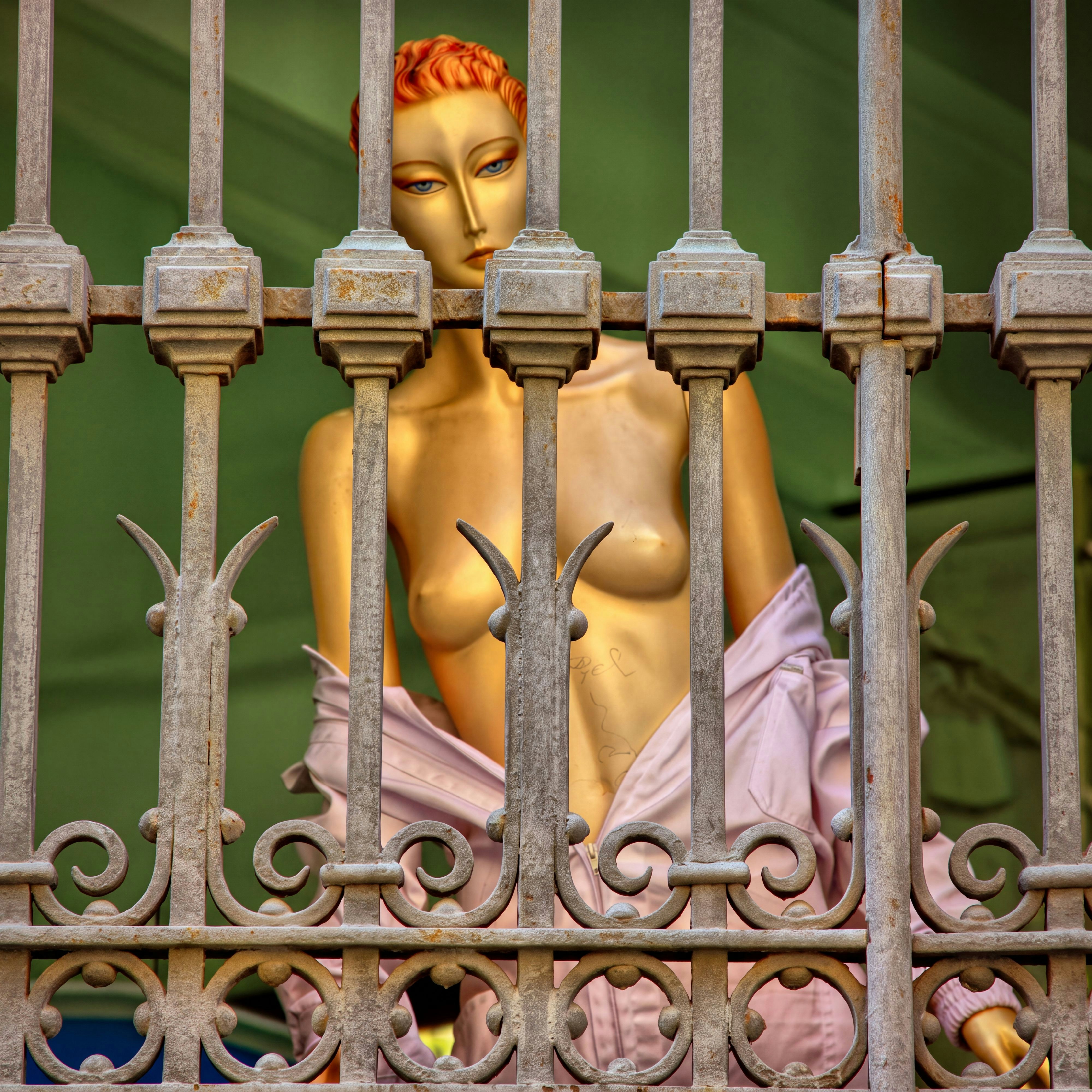 Un mannequin doré portant une veste rose pâle derrière une clôture métallique décorative