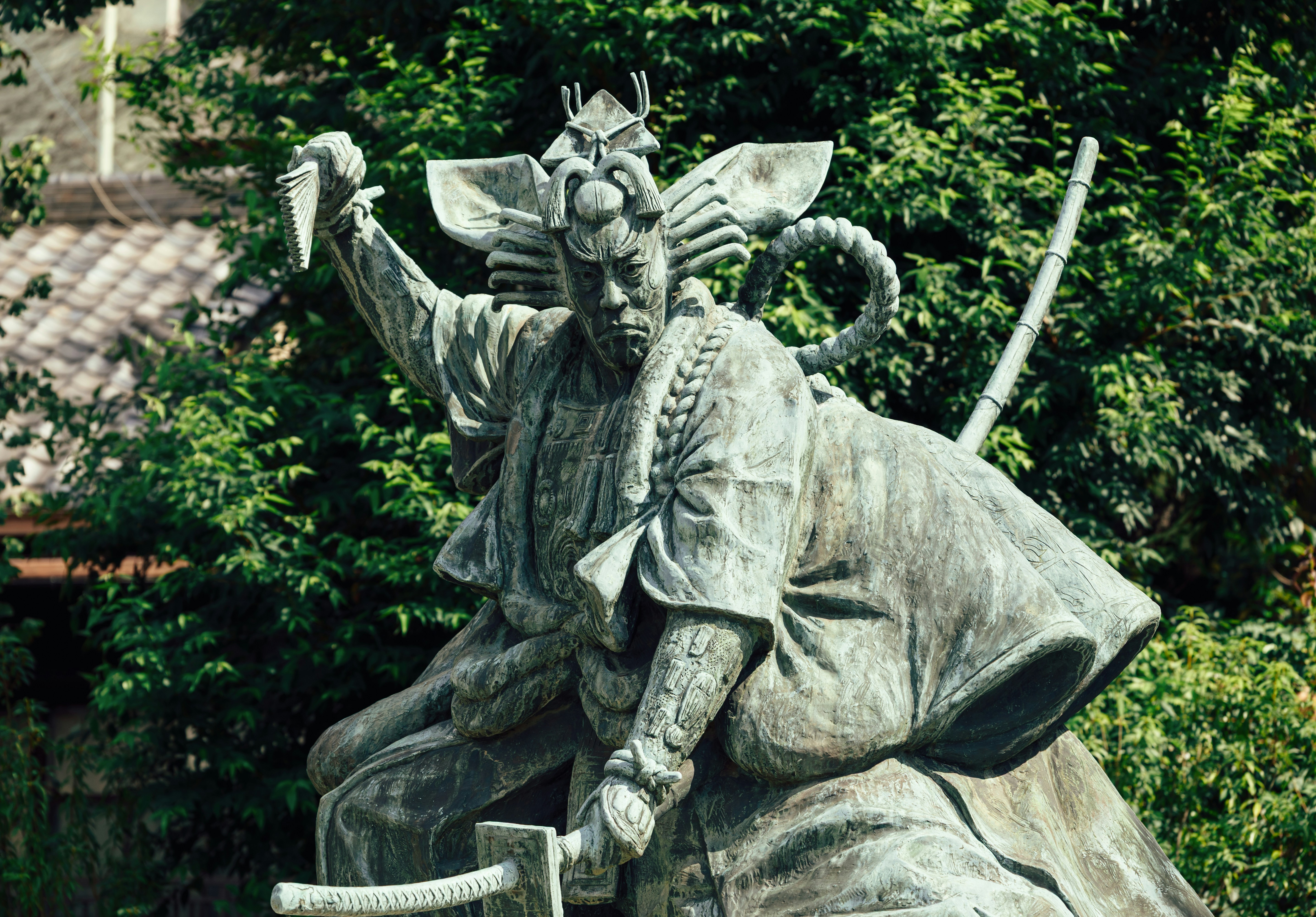 Une statue en bronze d’un guerrier samouraï tenant une épée sur un feuillage vert