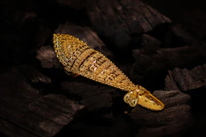 An ornate gold ring shaped like a fish resting on dark charcoal pieces