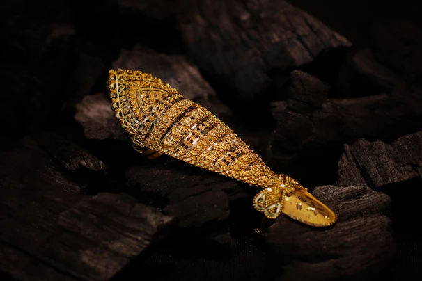 An ornate gold ring shaped like a fish resting on dark charcoal pieces