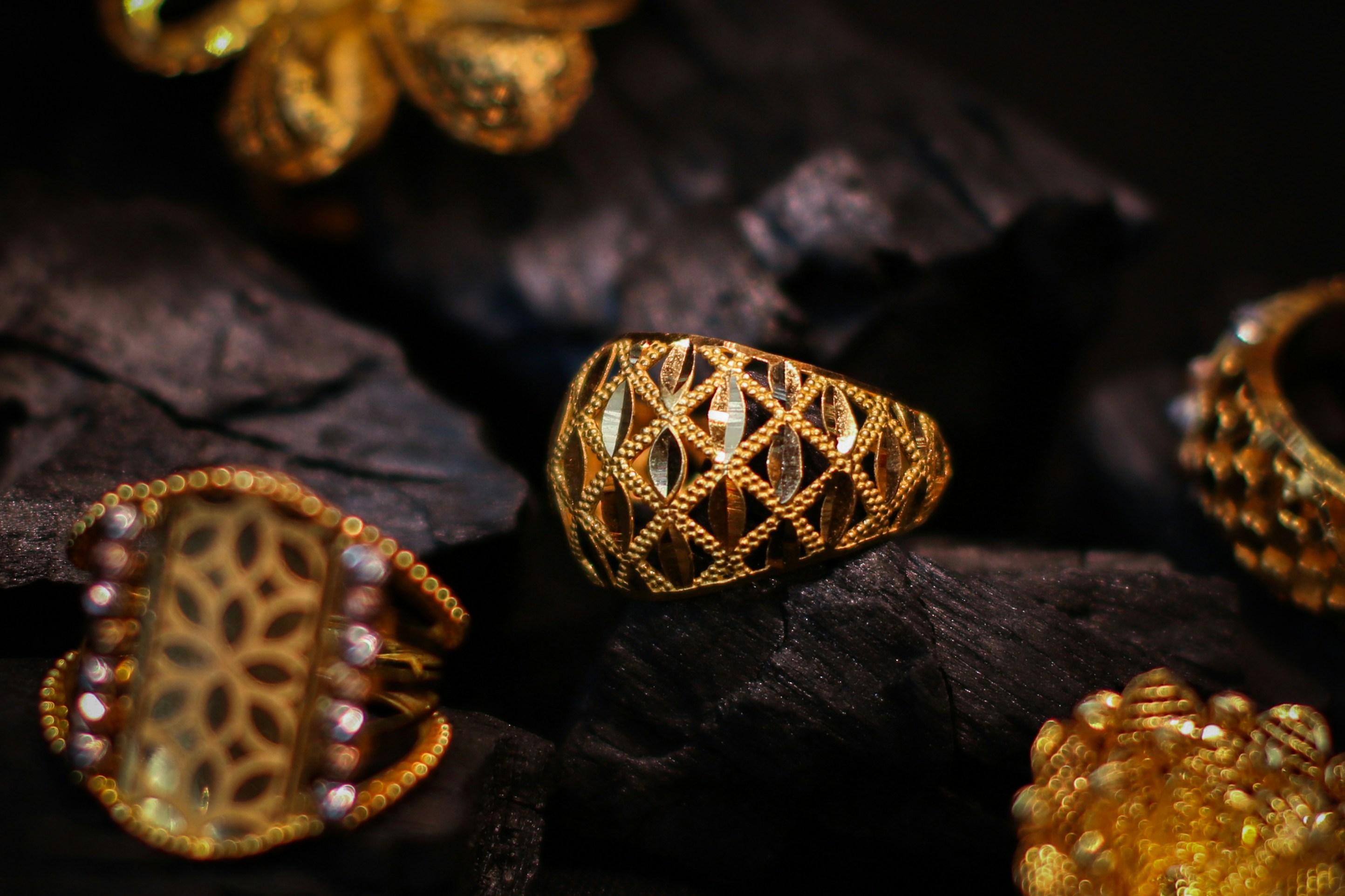 Four ornate gold rings resting on dark textured charcoal pieces