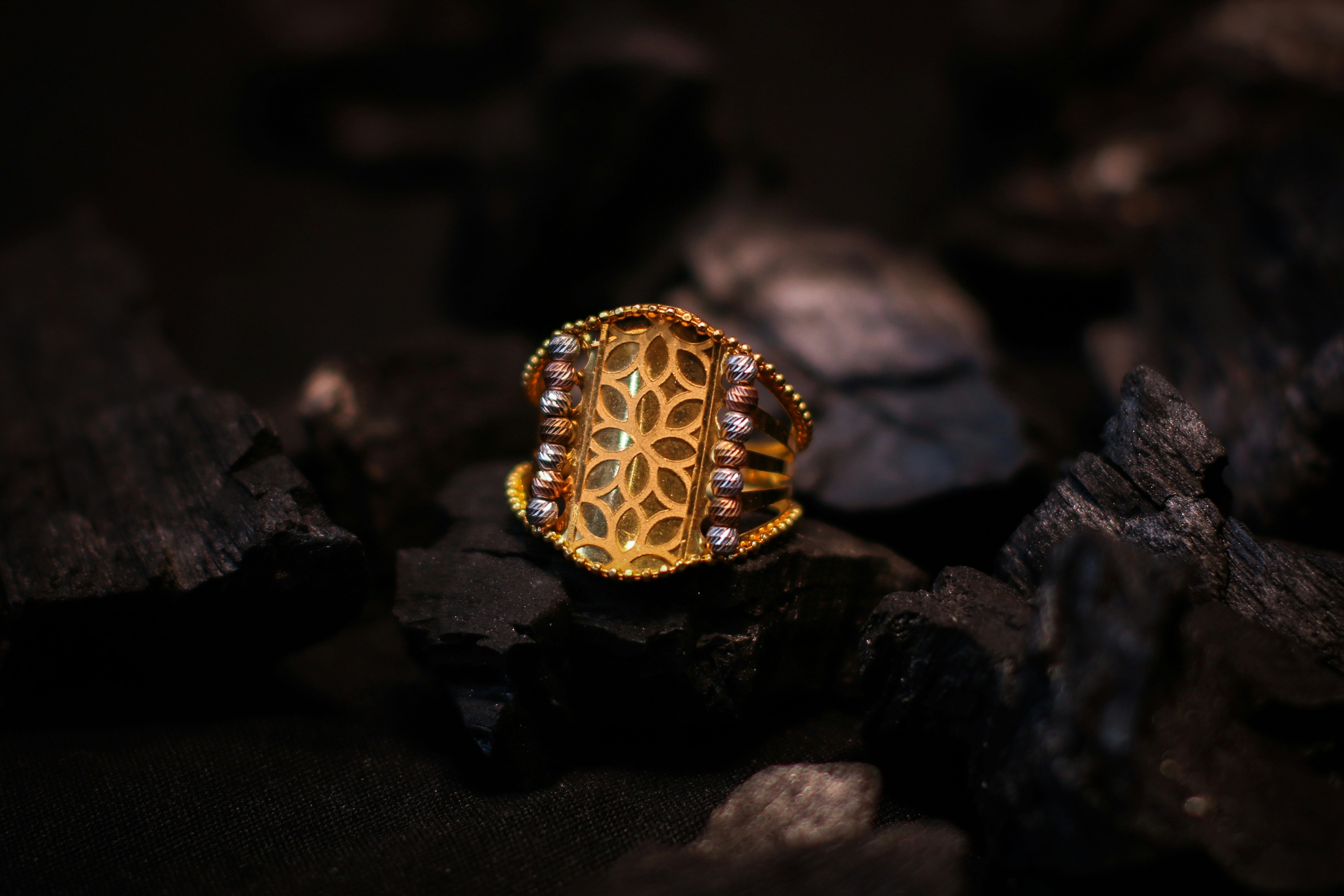 A gold ring with a patterned center resting on dark charcoal pieces