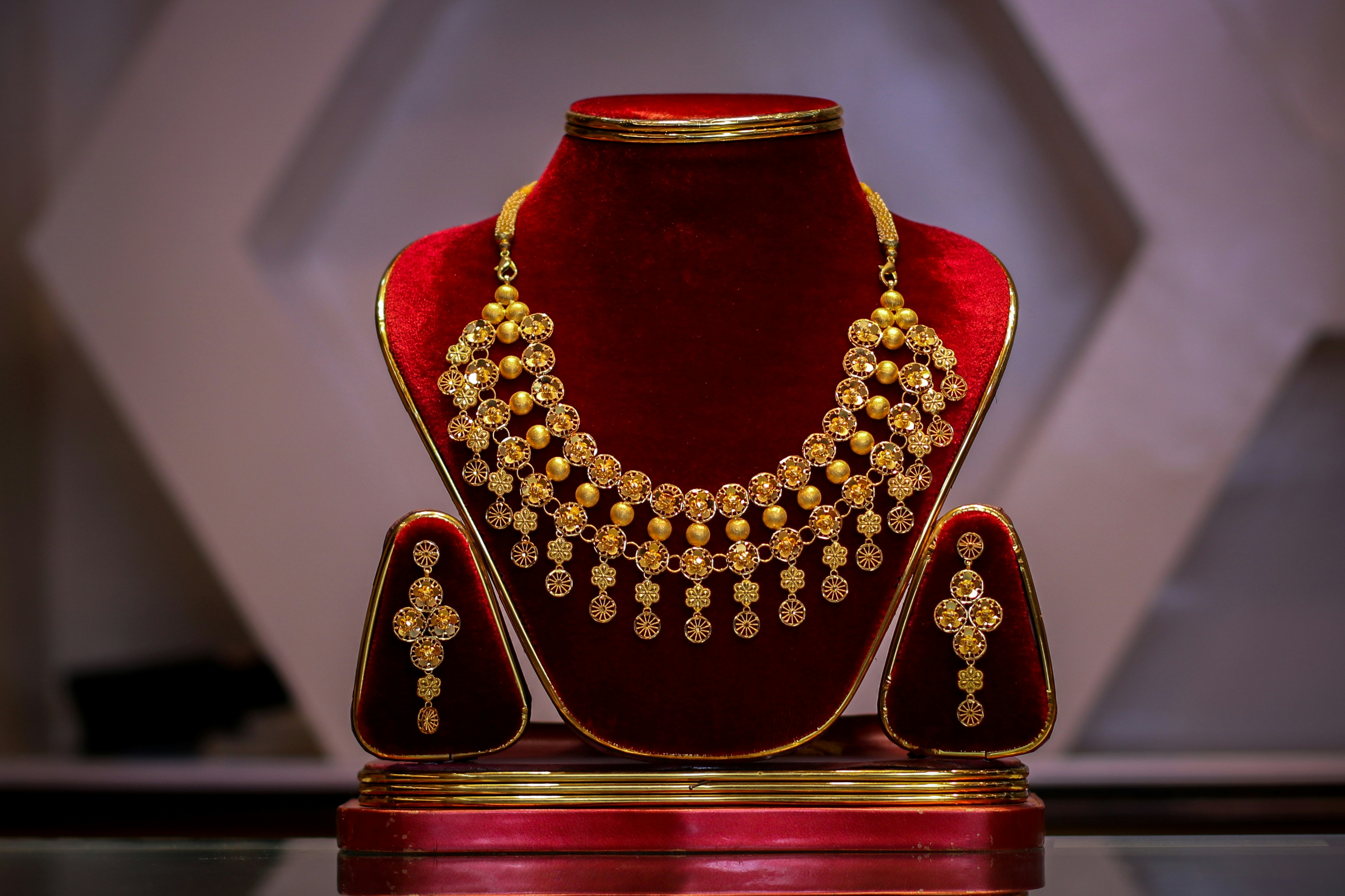 A gold necklace and matching earrings displayed on red velvet jewelry stands