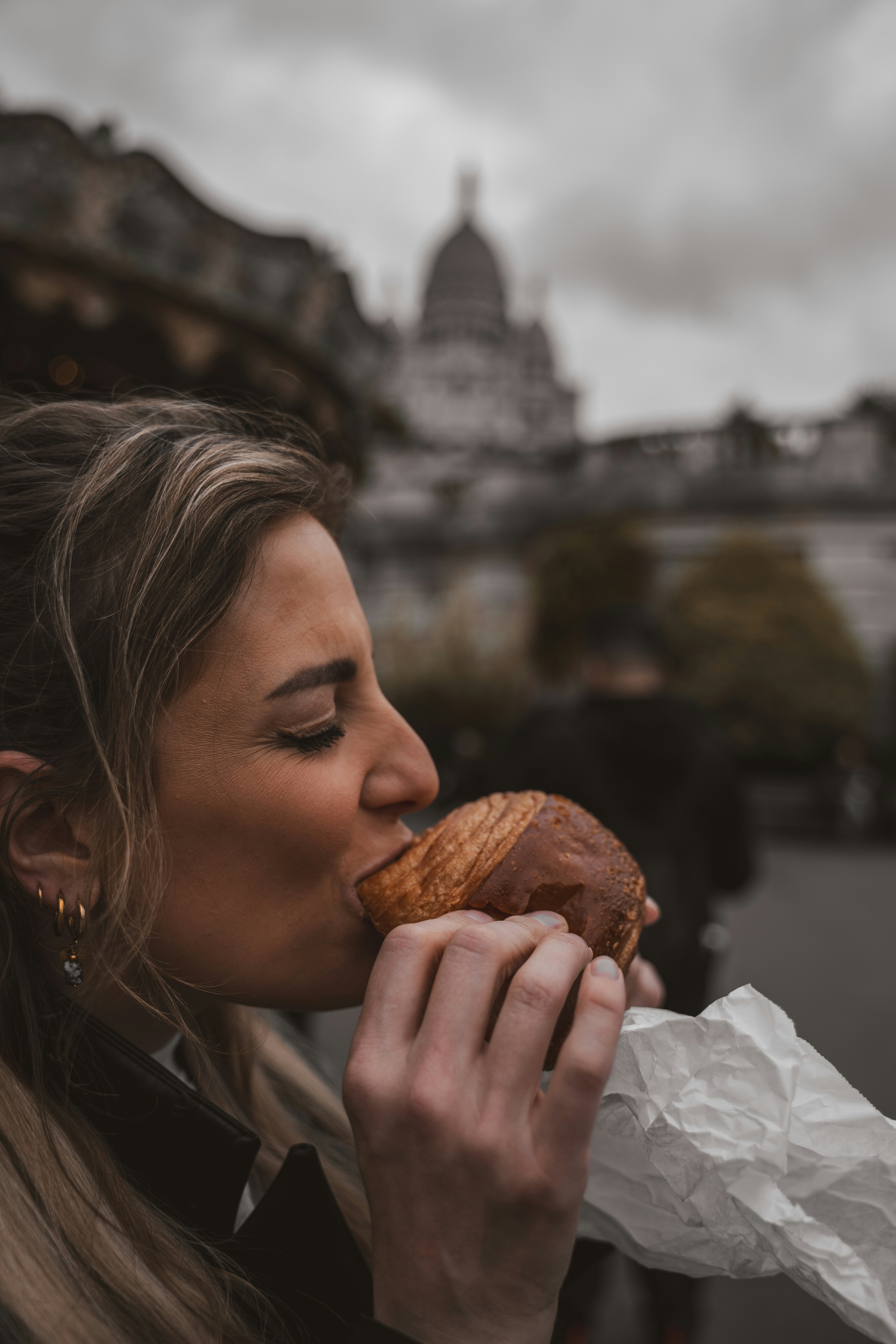 Uma mulher comendo um croissant em frente à Basílica do Sacré-Cœur em Paris