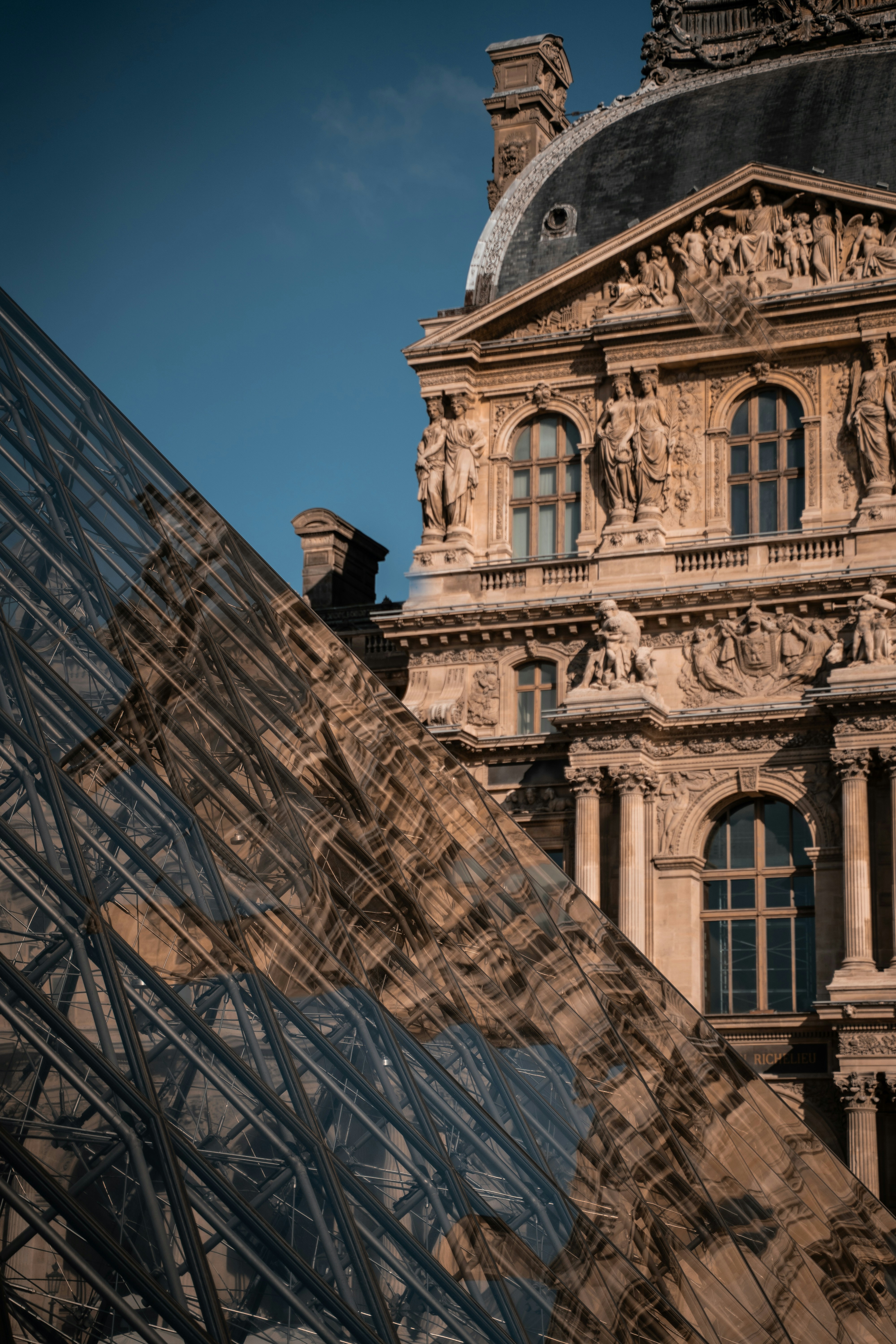 A Pirâmide de vidro do Louvre refletindo a ornamentada fachada de pedra do Museu do Louvre em Paris