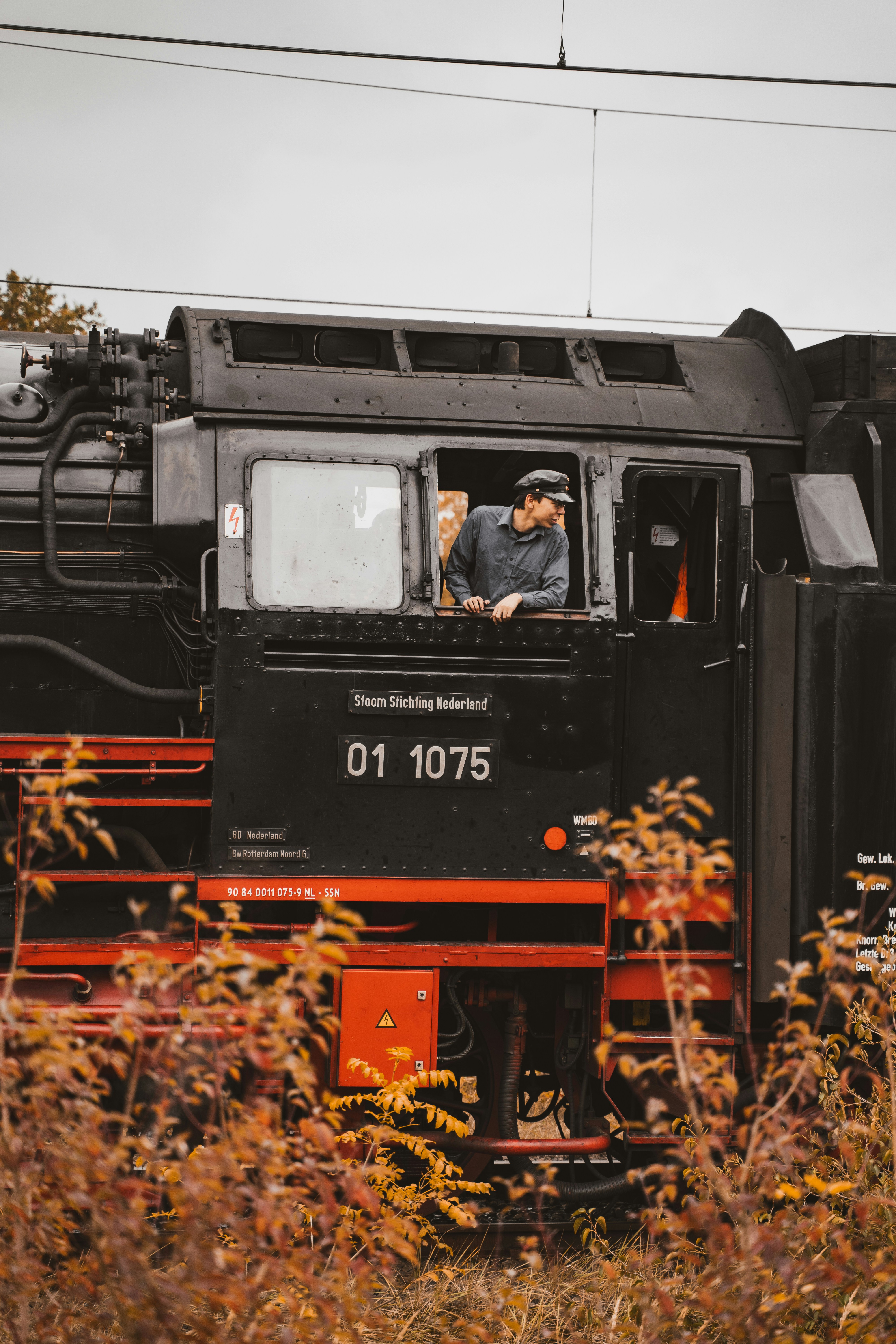 Uma pessoa de boné olhando de uma cabine preta de locomotiva a vapor