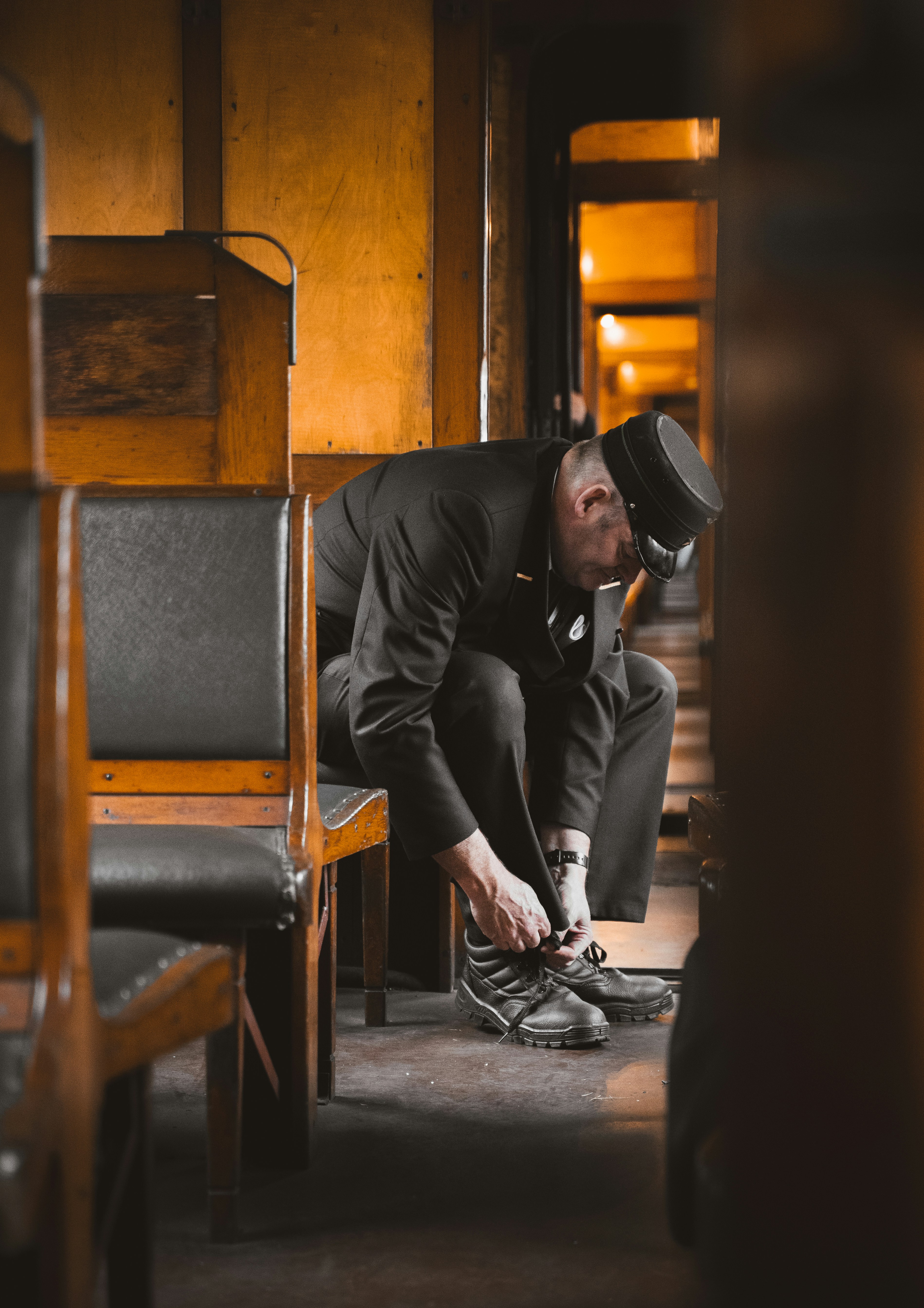 Um homem de uniforme escuro e boné amarrando as botas em um trem