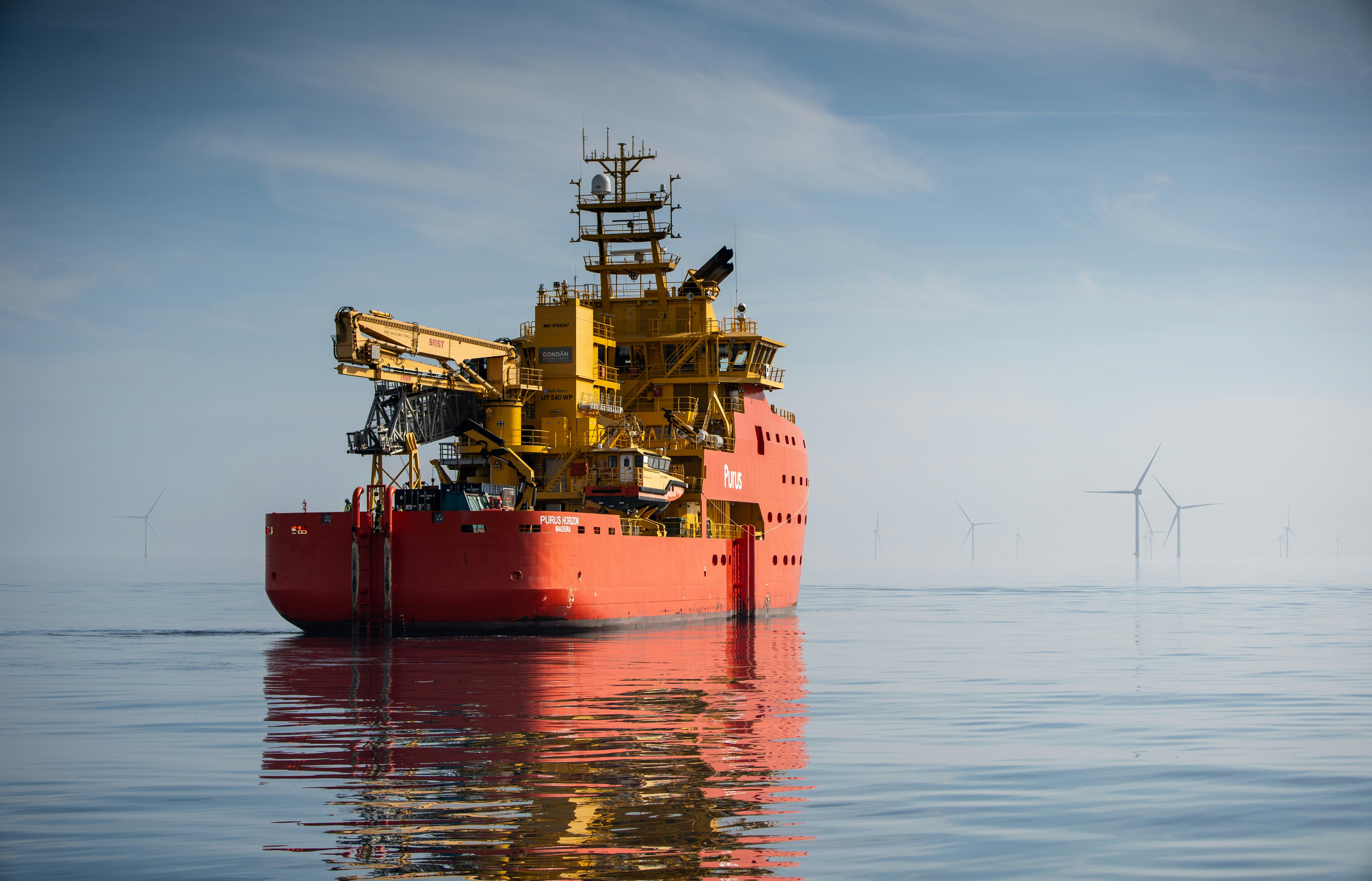 Um navio de apoio offshore vermelho e amarelo em águas calmas próximas a turbinas eólicas