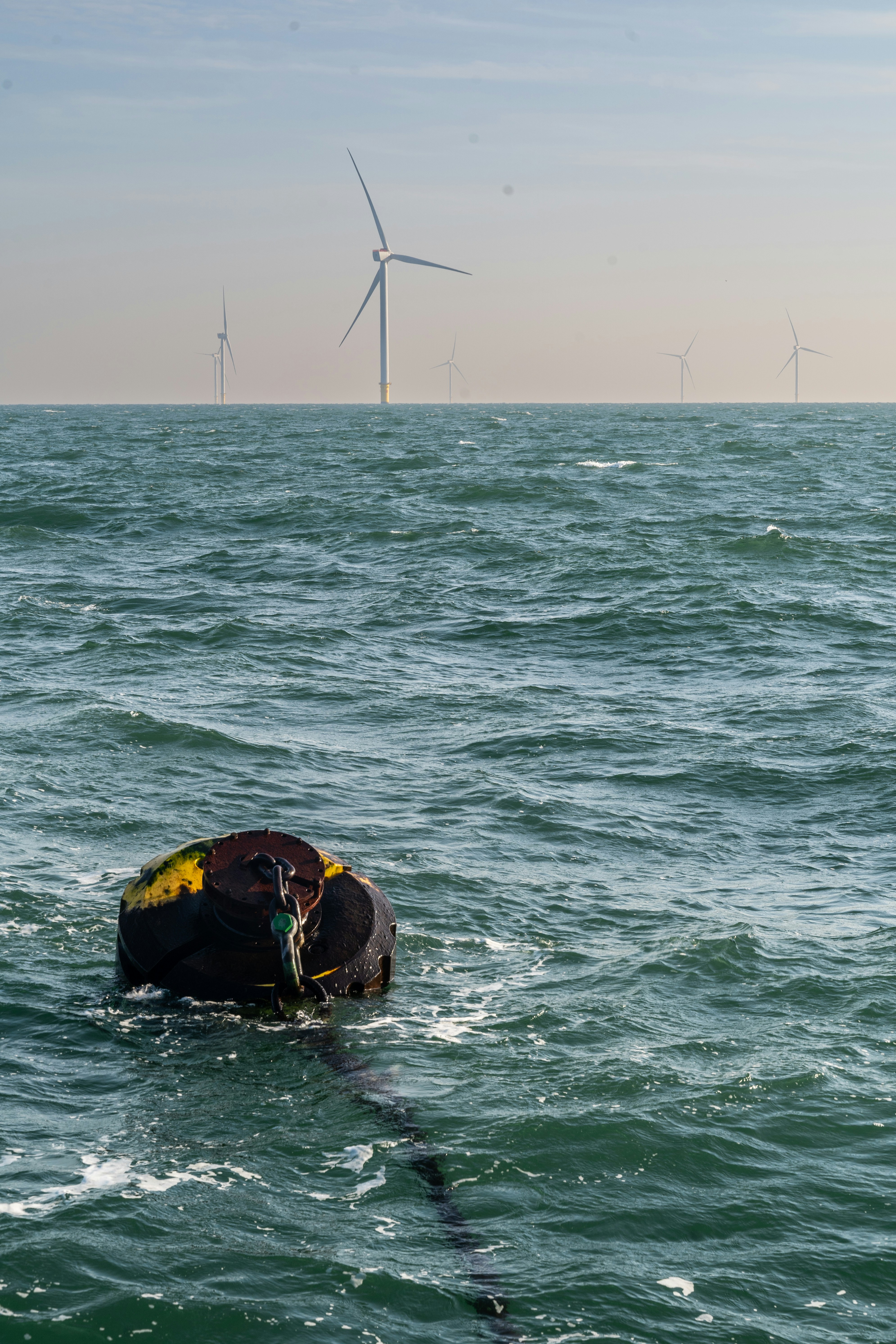 Uma bóia escura de amarração flutuando no mar agitado com turbinas eólicas offshore