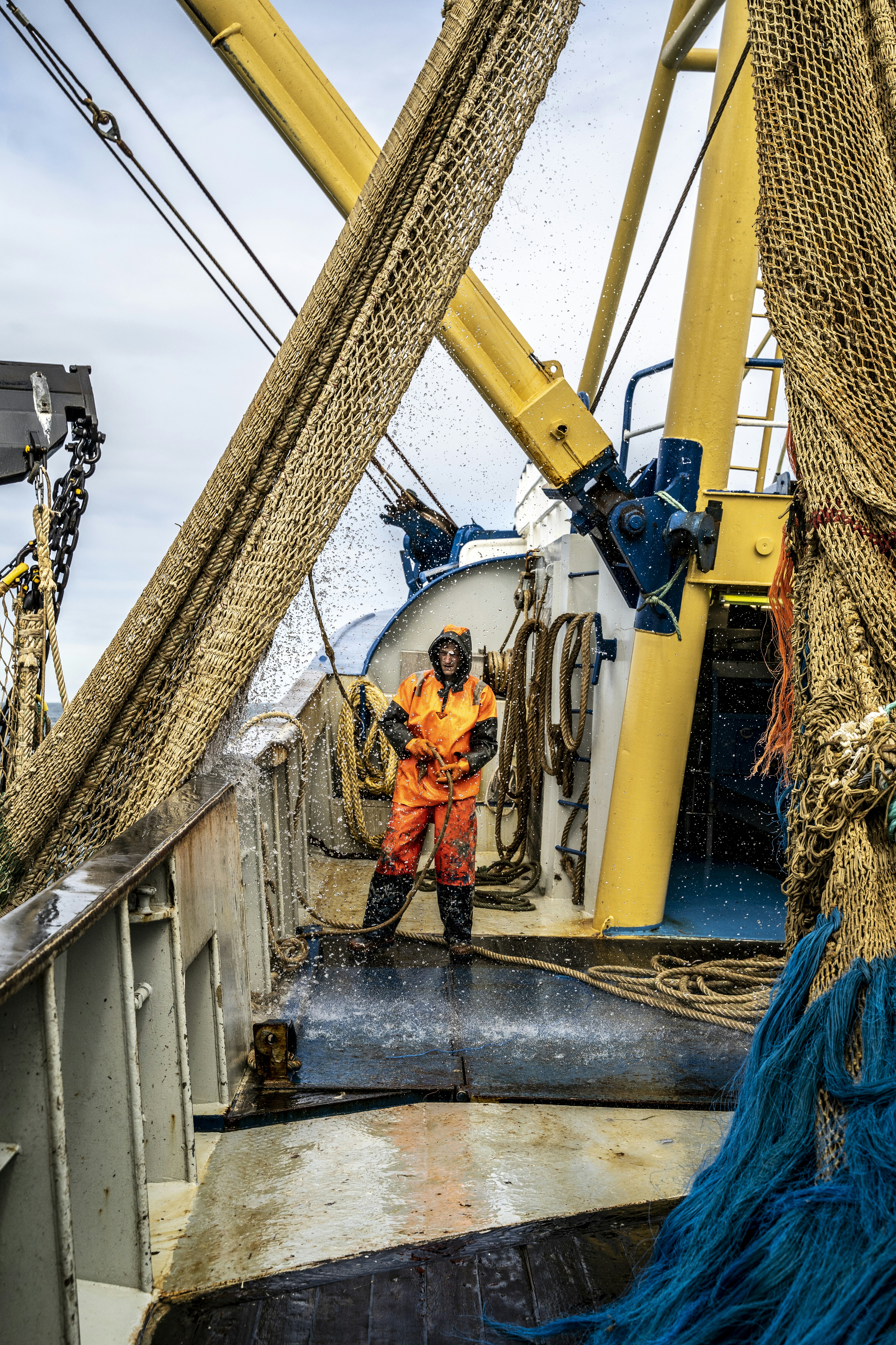 Uma pessoa com roupas impermeáveis laranja puxando uma corda no convés de um barco de pesca
