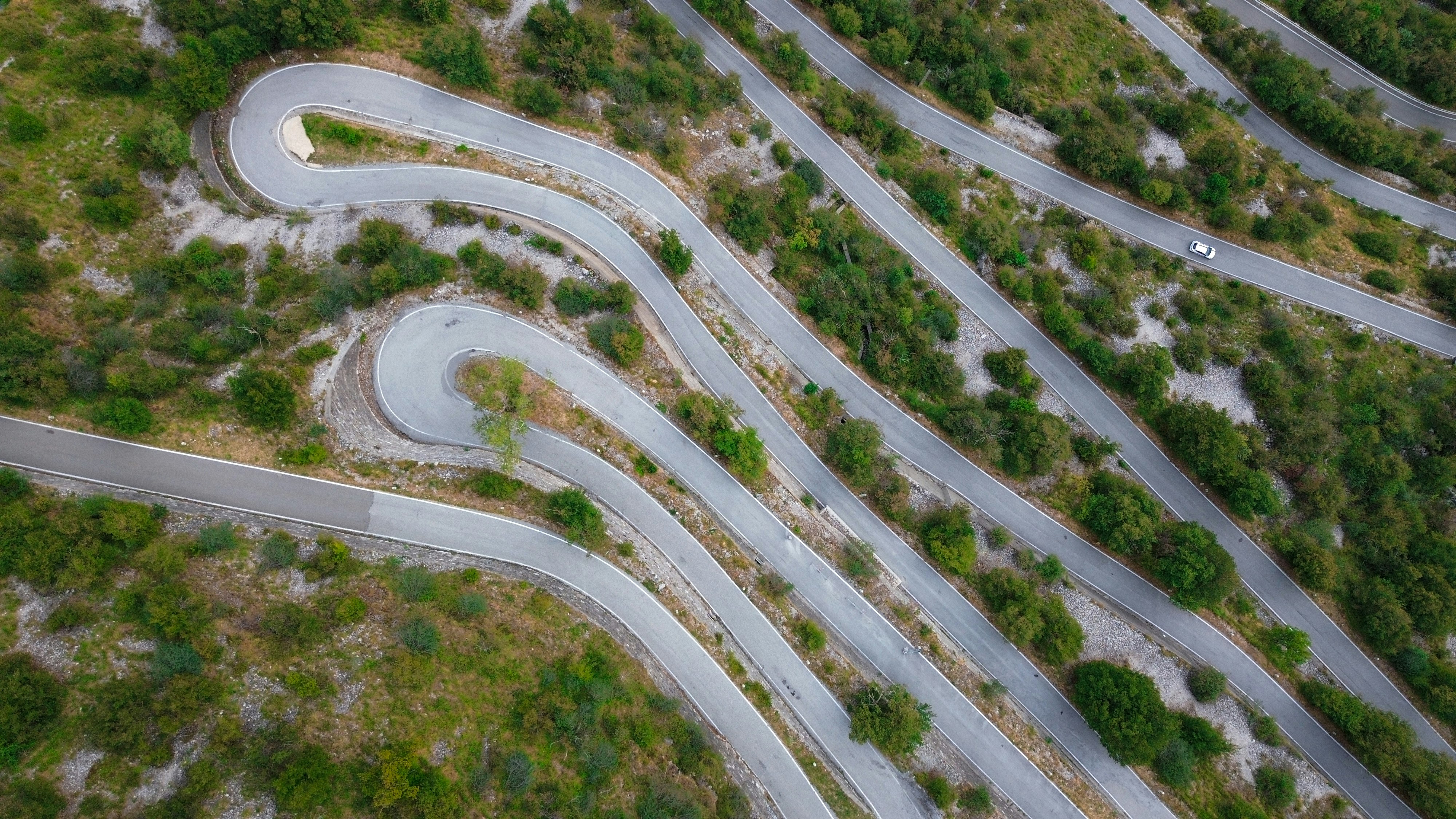 An aerial view of a winding mountain road with hairpin turns through green vegetation
