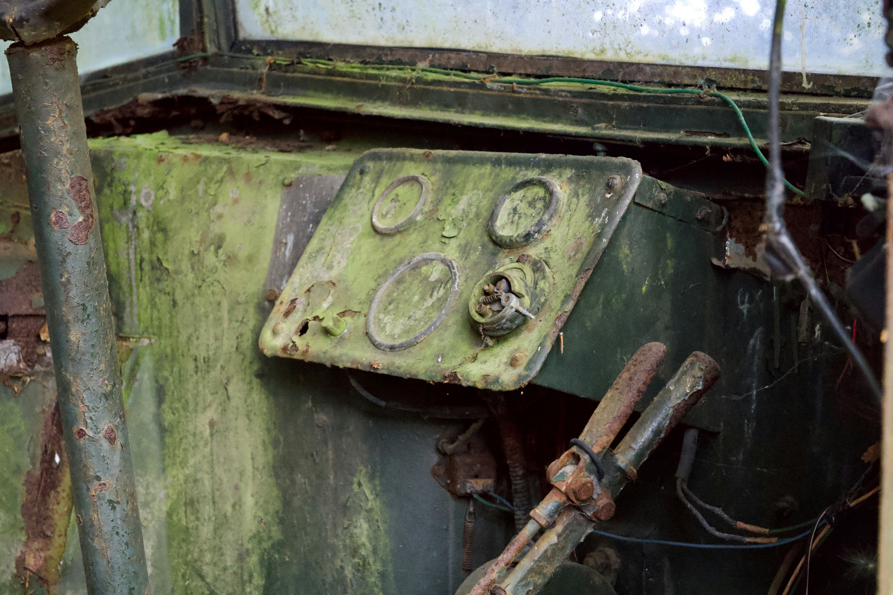 A rusted green dashboard with circular gauges inside an abandoned vehicle