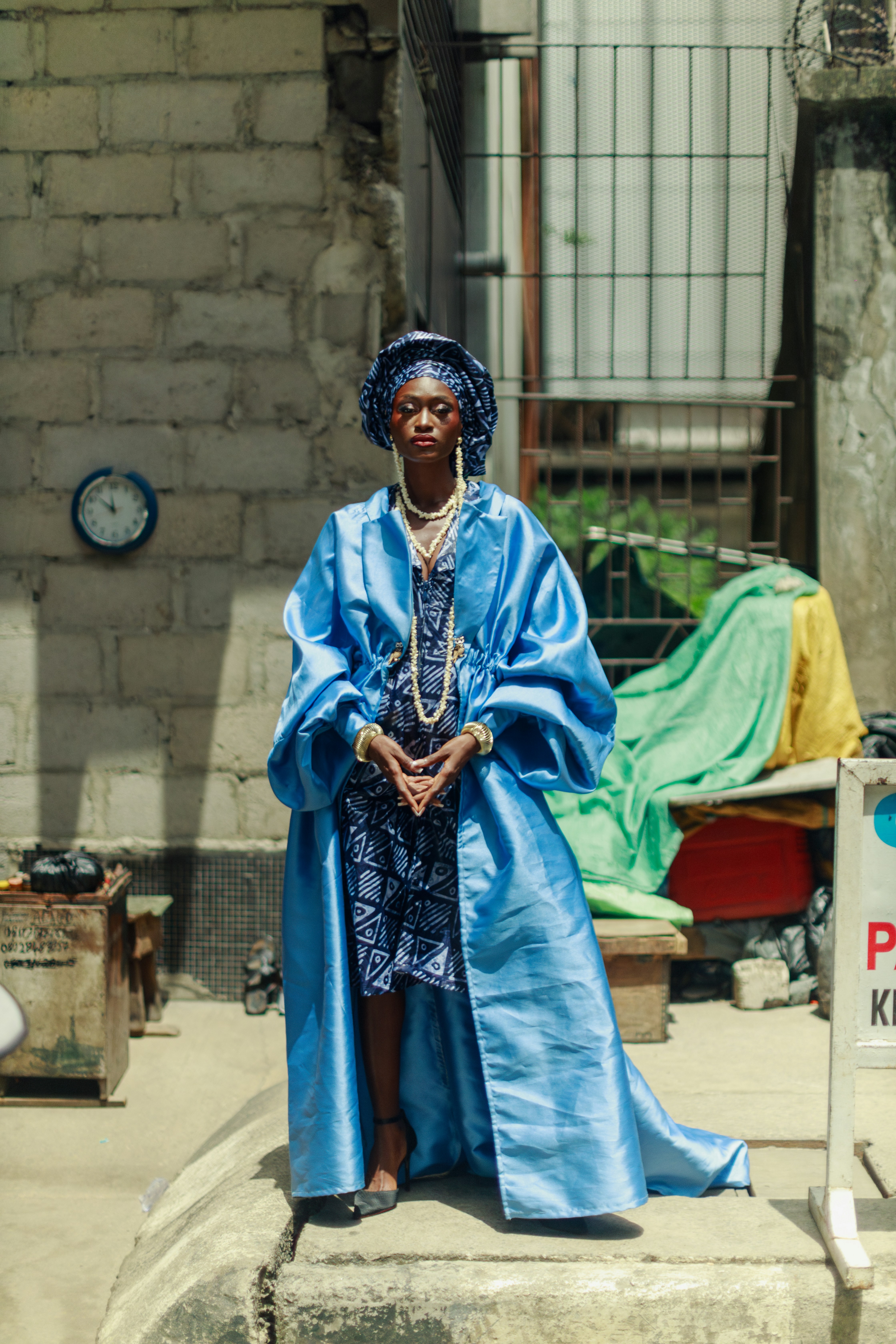 A woman in a blue satin coat and patterned dress in Lagos, Nigeria
