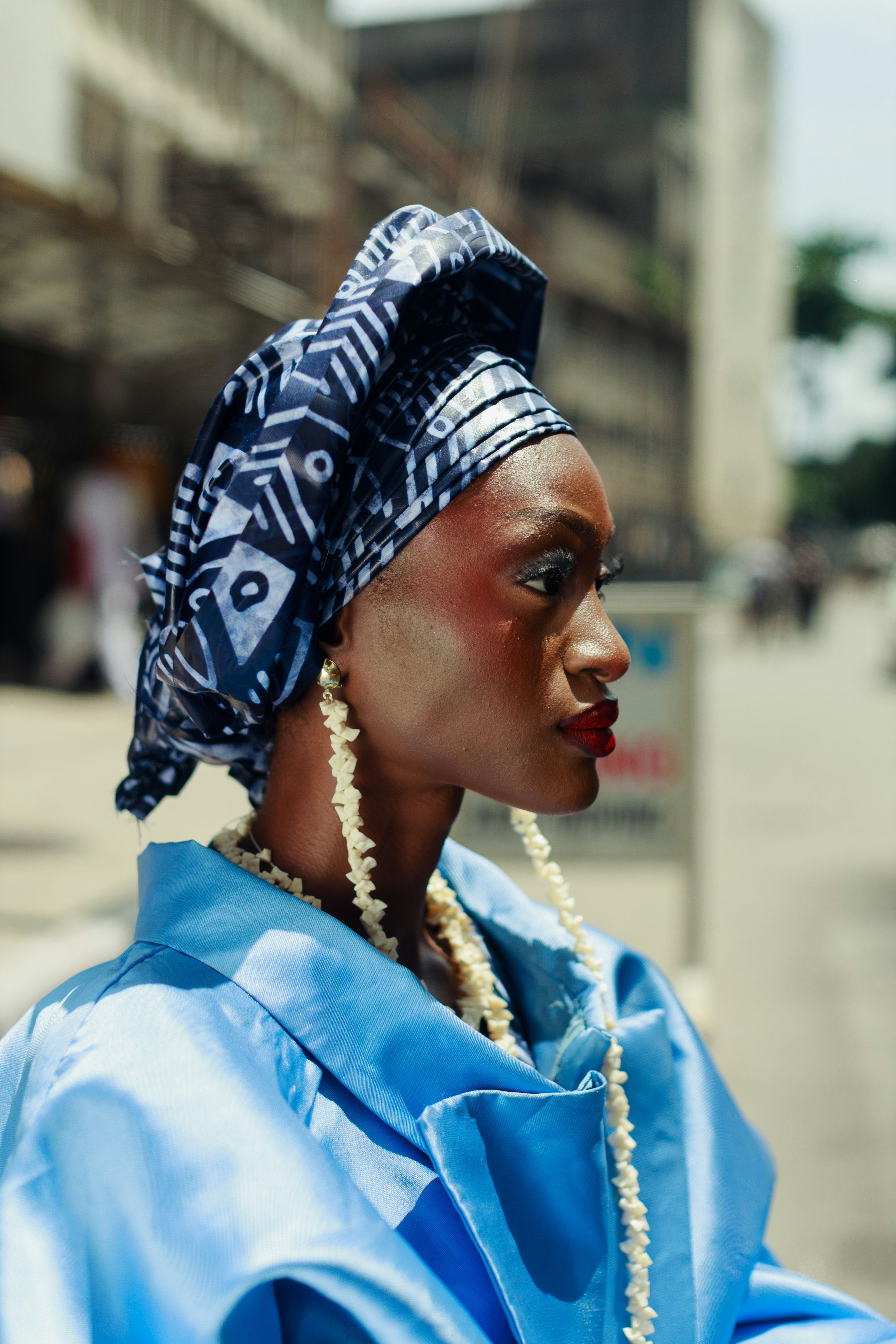 A woman in a blue headwrap and jacket with long shell earrings in Lagos