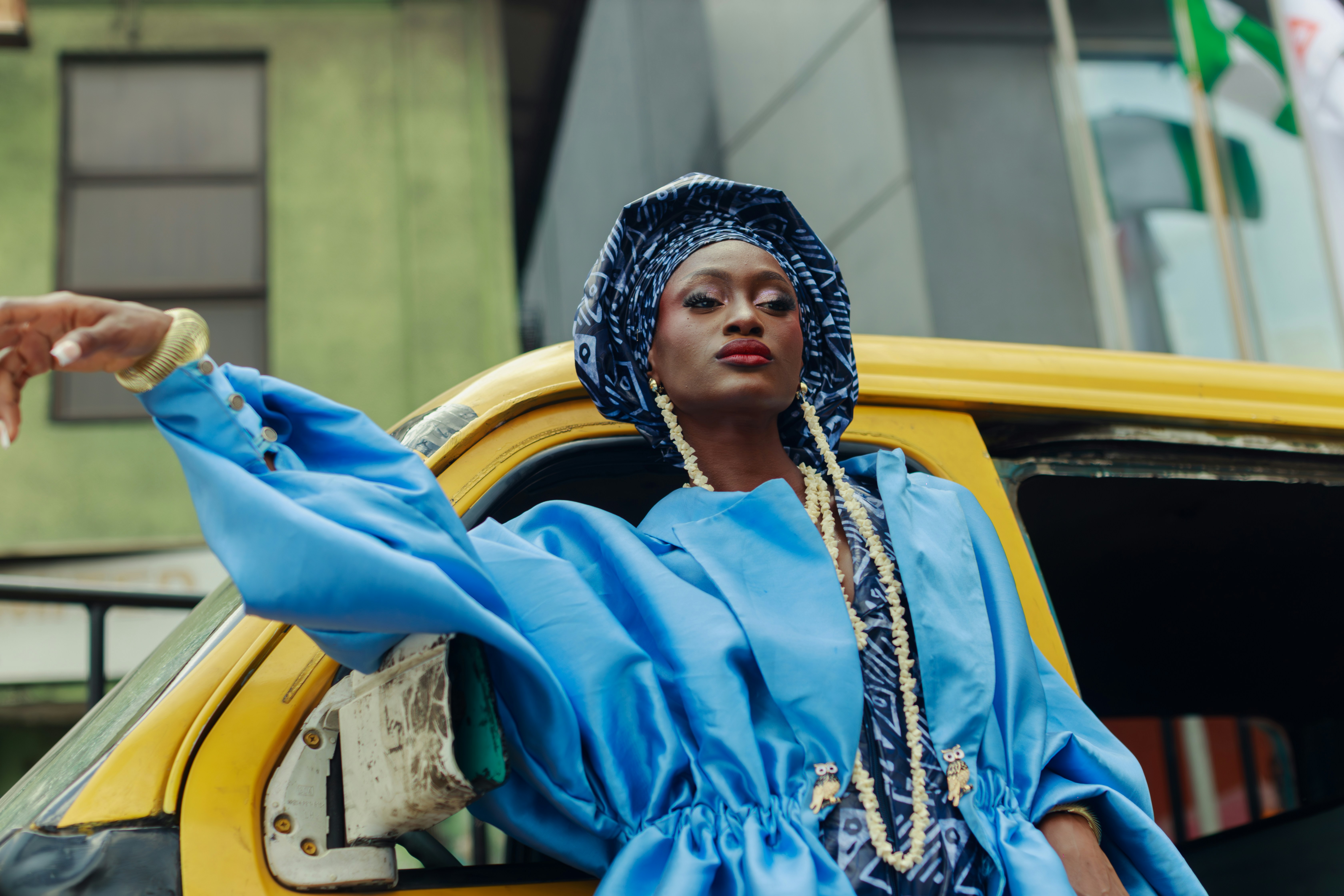 A woman in a blue jacket and headwrap by a yellow bus in Lagos