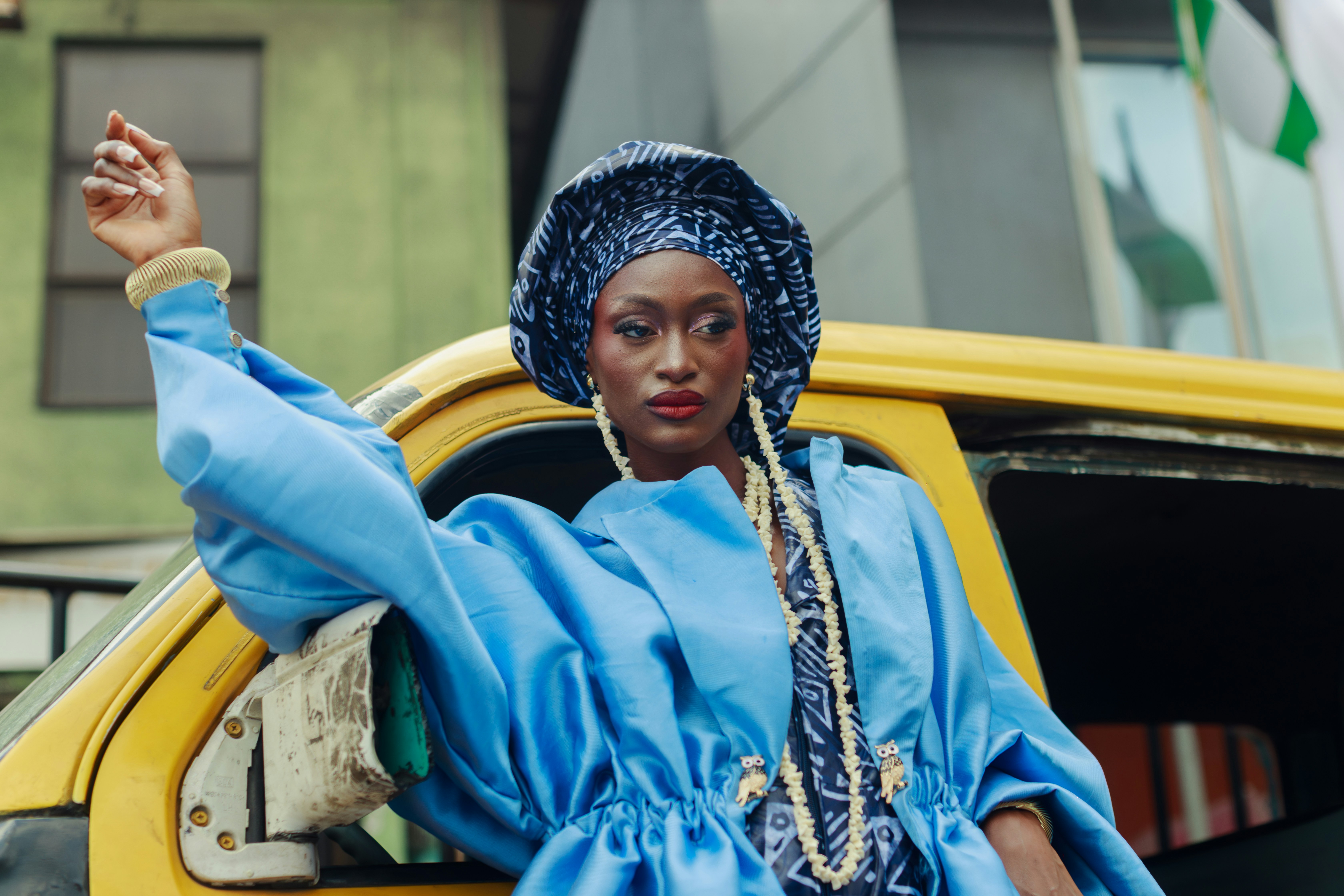 Uma mulher de casaco azul e faixa de cabeça posando ao lado de um ônibus amarelo em Lagos